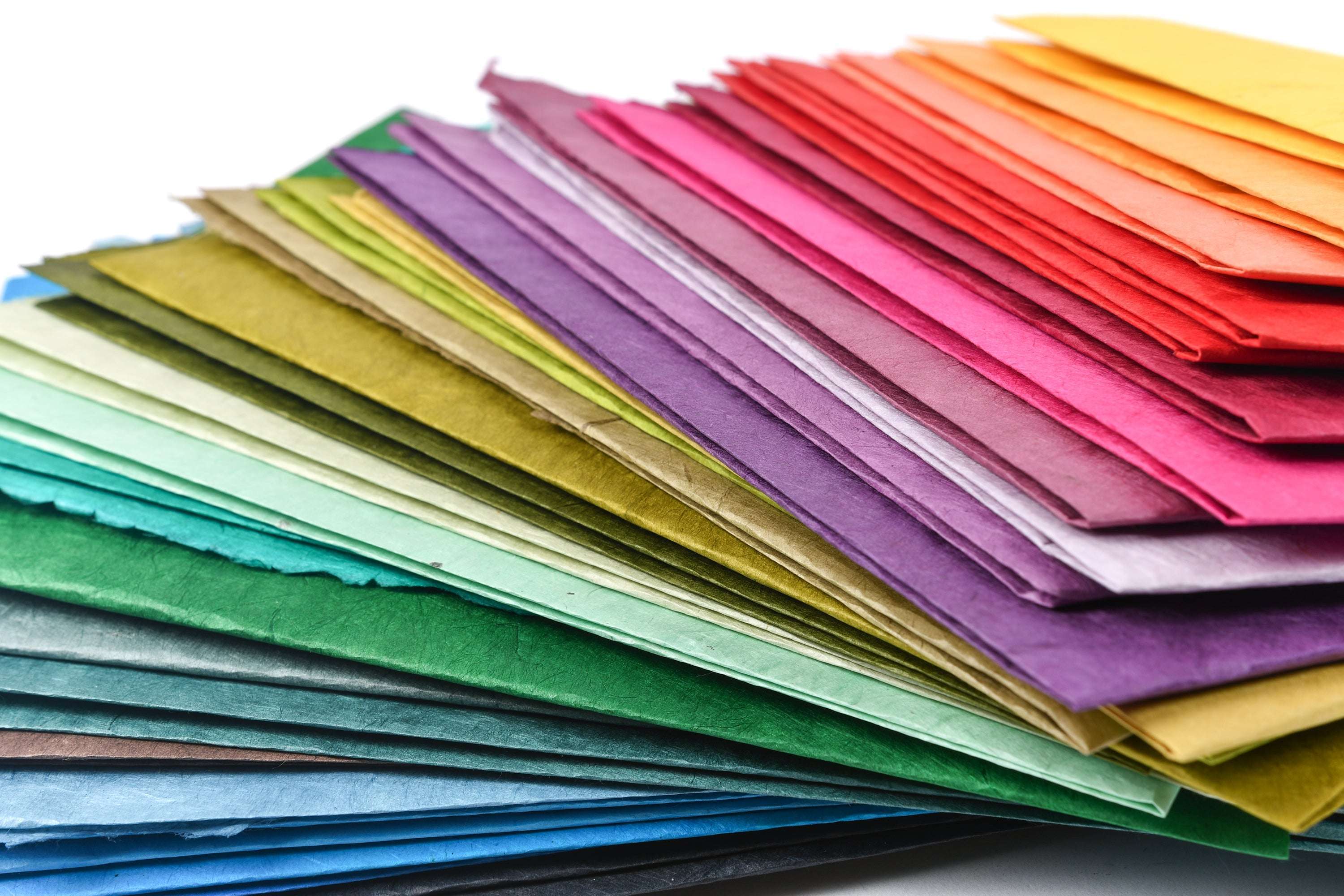 Stapel blasspfirsichfarbener handgeschöpfter Papiere, eines davon mit weißem Blumenmuster, angeordnet auf einer weißen Fläche.