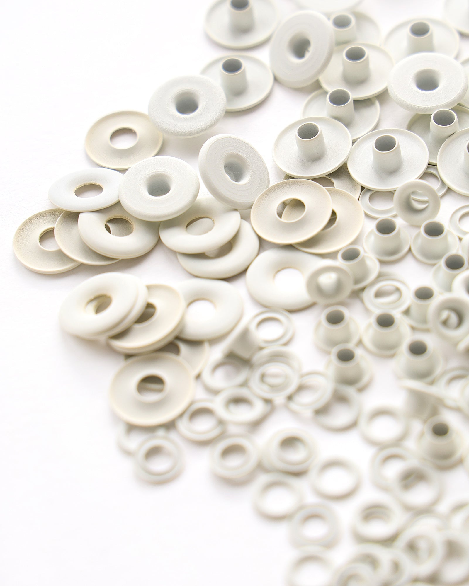 Nahaufnahme von verstreuten weißen Metallscheiben und Ösen auf einer weißen Fläche.