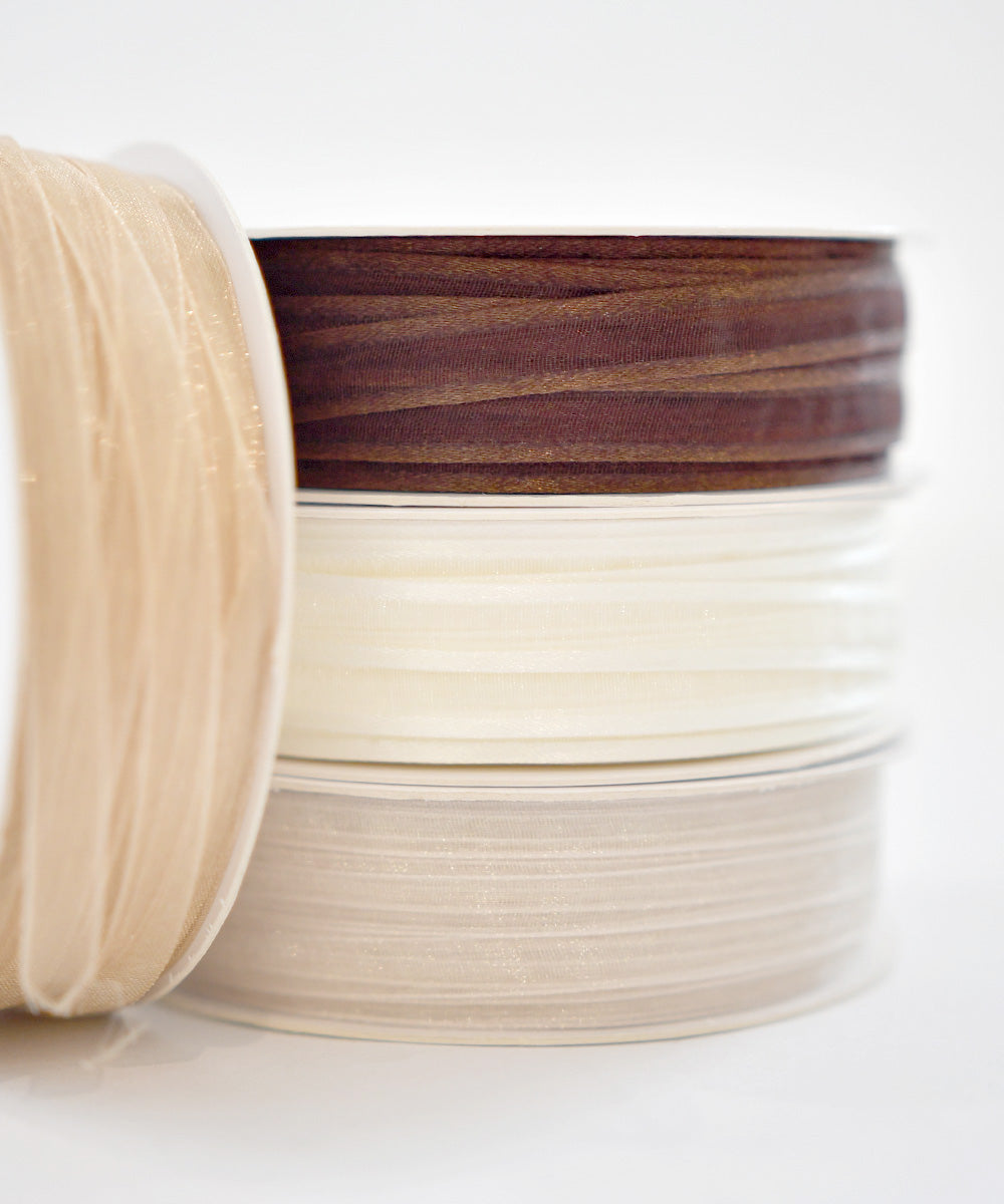 Vier Spulen mit durchsichtigem Band in Beige, Braun, Weiß und Elfenbein auf weißem Hintergrund.