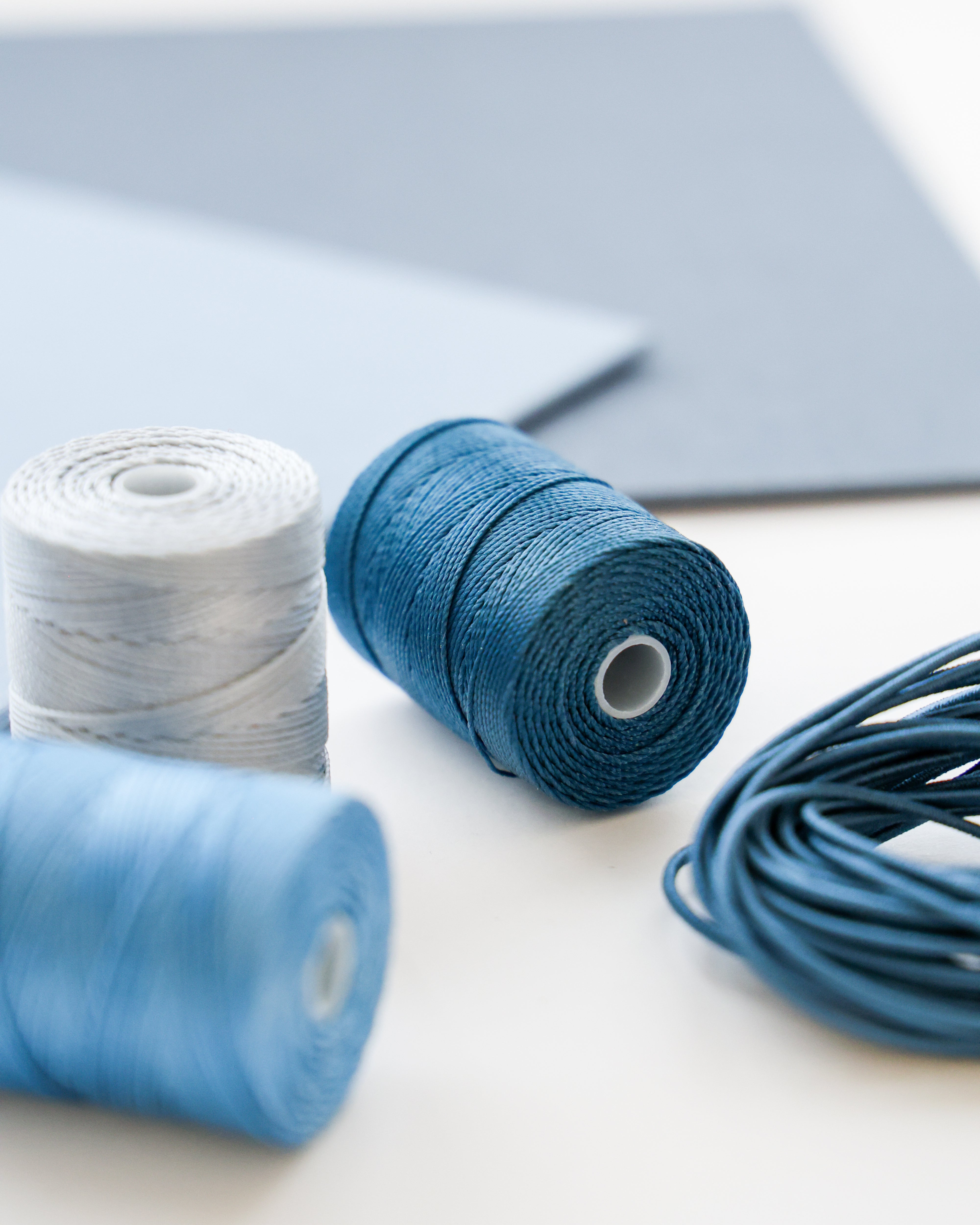 Drei Spulen mit blauem und weißem Garn mit blauer Kordel und blauen Papierbögen im Hintergrund.