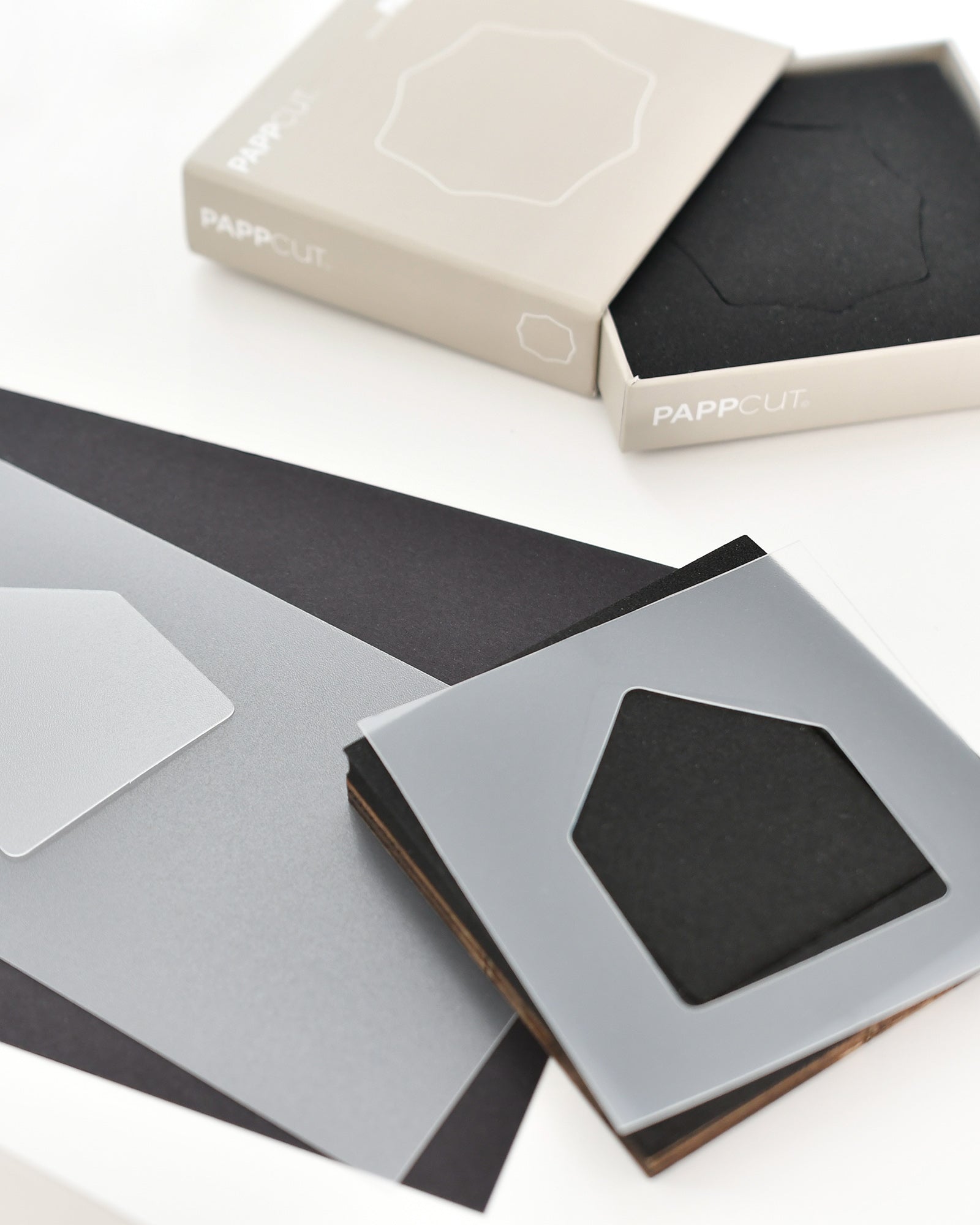 Minimalistische Schreibwaren, darunter schwarzes und graues Papier und geometrische Untersetzer, die mit Verpackungen ausgestellt werden.