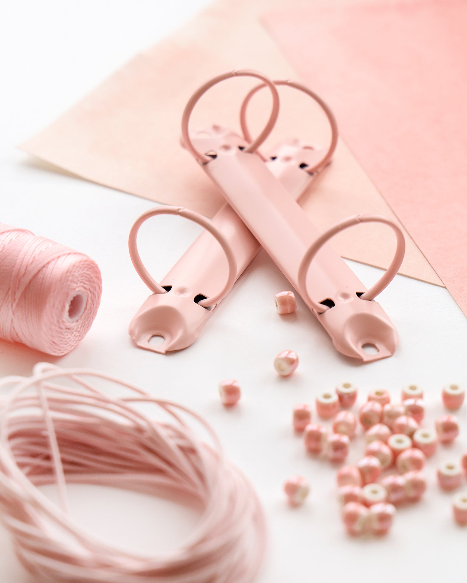 Rosa Binderinge, Schnur, Papier und Perlen ordentlich auf einer weißen Fläche zum Basteln angeordnet.