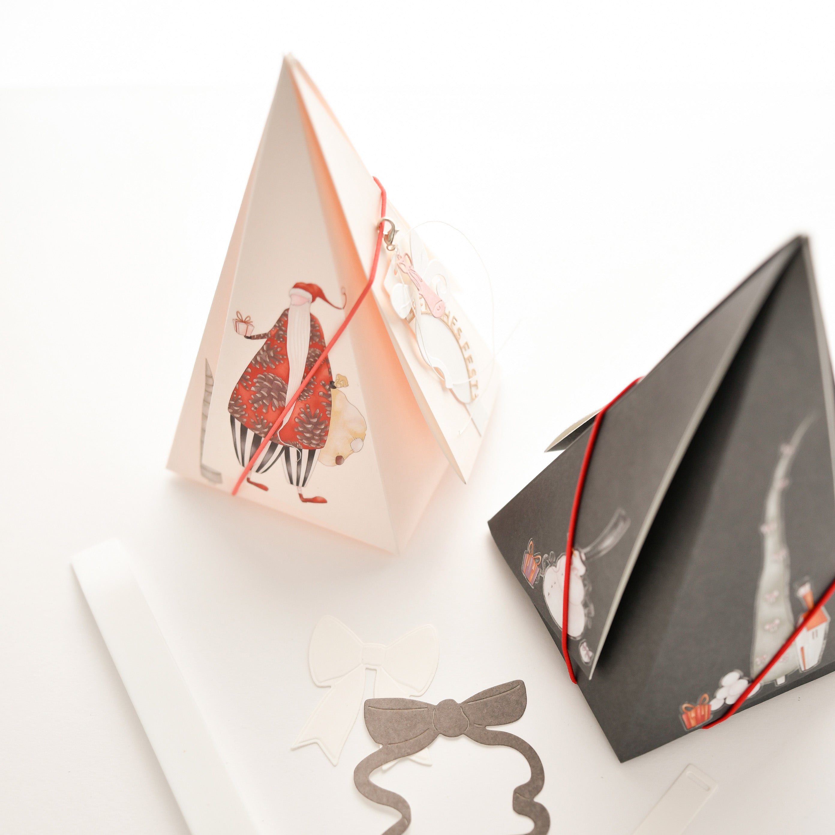 Zwei dreieckige Geschenkschachteln, eine weiße und eine schwarze, verziert mit weihnachtlichen Illustrationen.