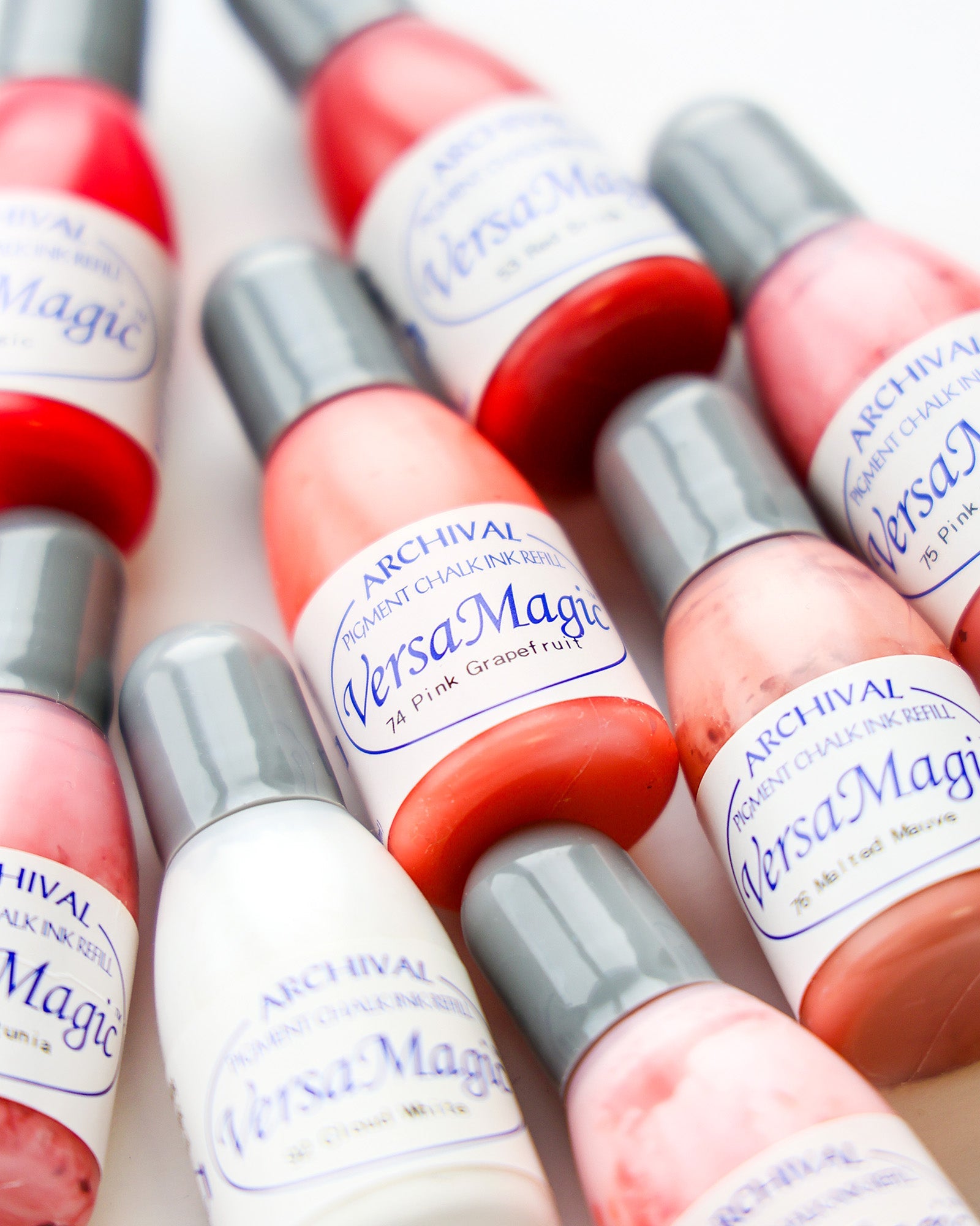 Mehrere Flaschen VersaMagic Archivpigmentkreidetinte in rosa, roten und weißen Farbtönen sind dicht nebeneinander angeordnet.