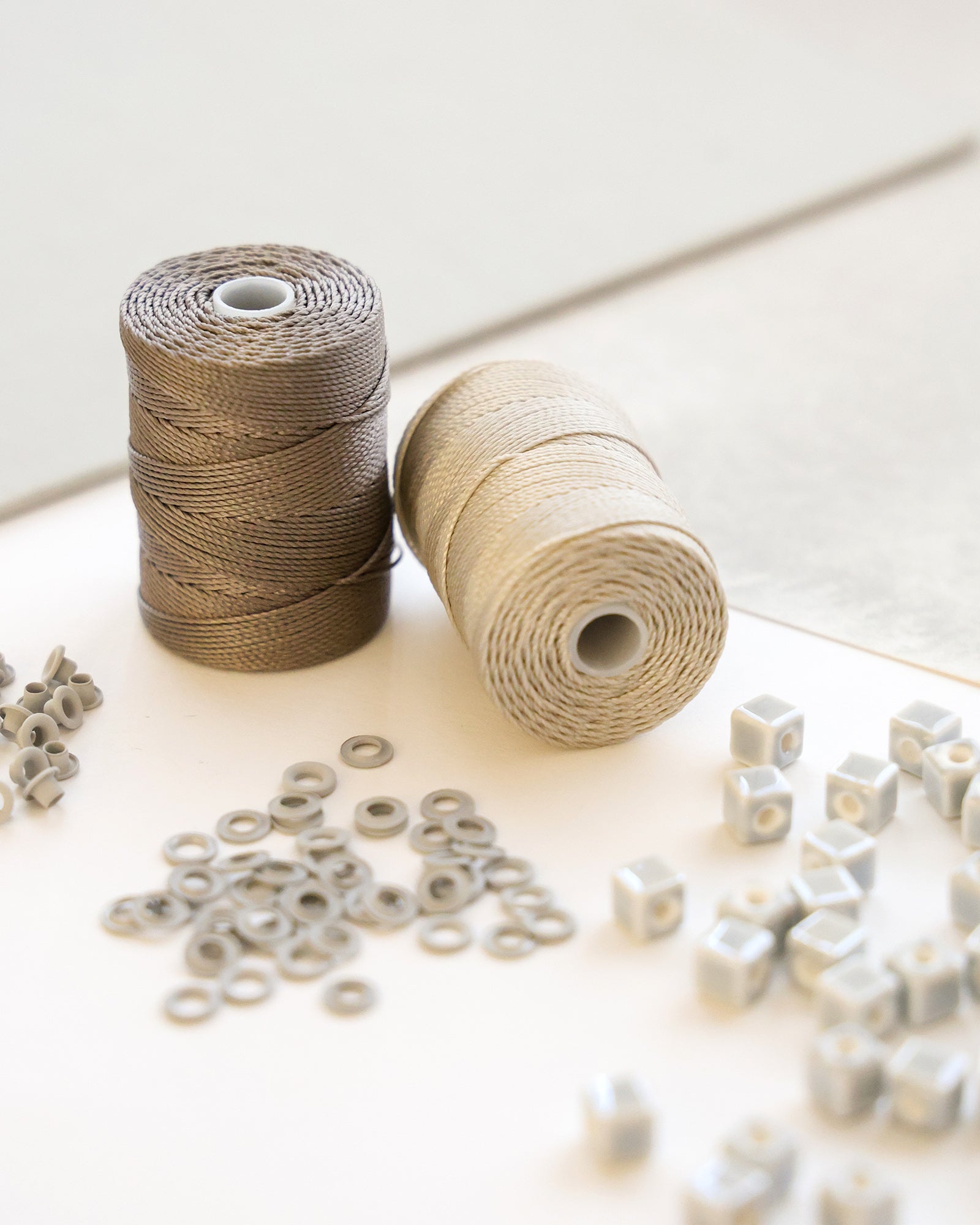 Zwei Garnspulen mit verstreuten kleinen grauen Perlen und Ringen auf einer hellen Oberfläche.