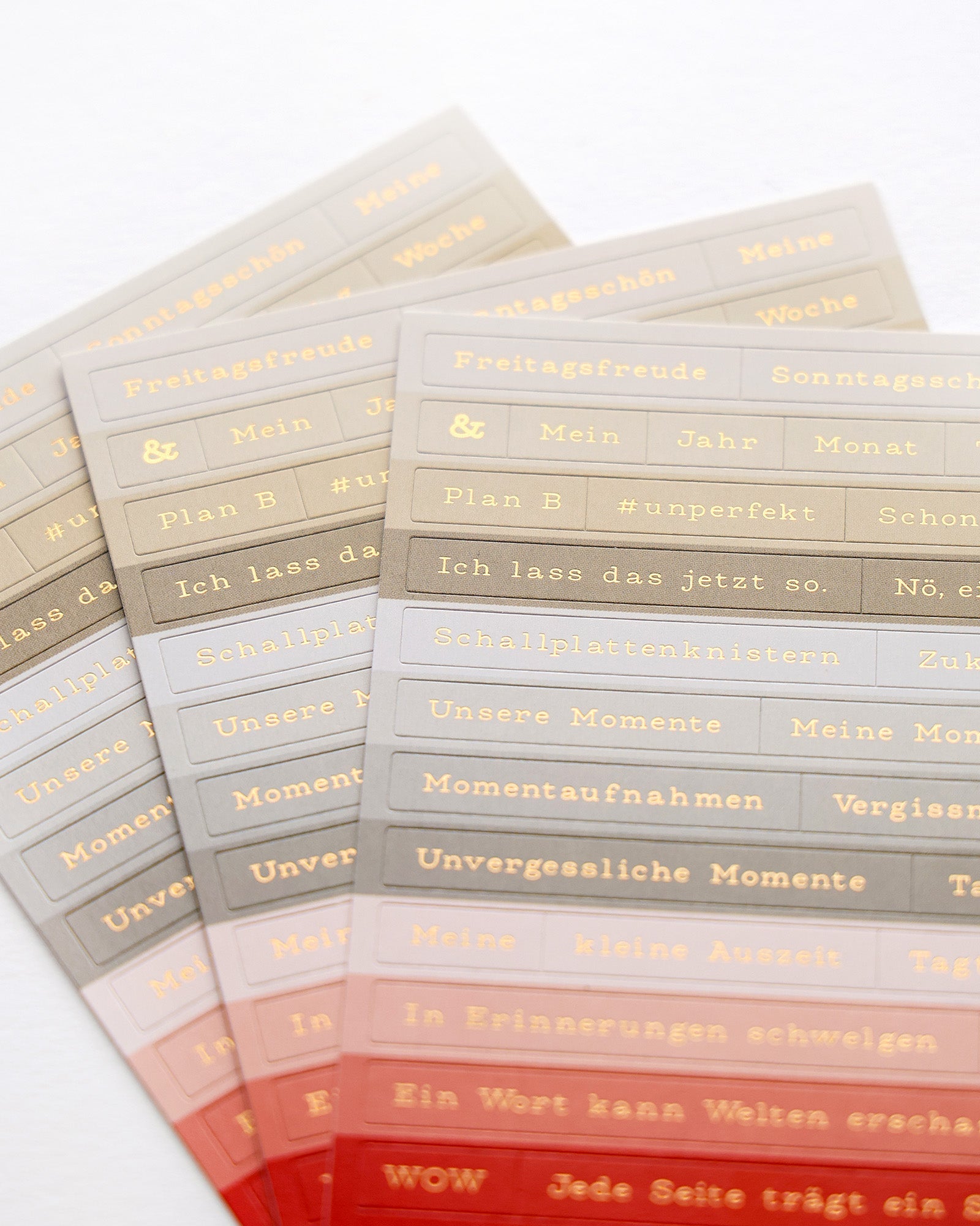 Pastellfarbene Aufkleberblätter mit deutschen Wörtern und goldenen Symbolen wie Herzen und Sternen.