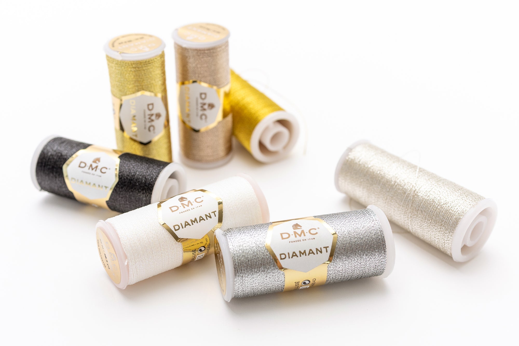 Acht Spulen DMC Diamant Metallic-Stickgarn in Gold, Silber, Schwarz und Weiß auf weißem Untergrund.