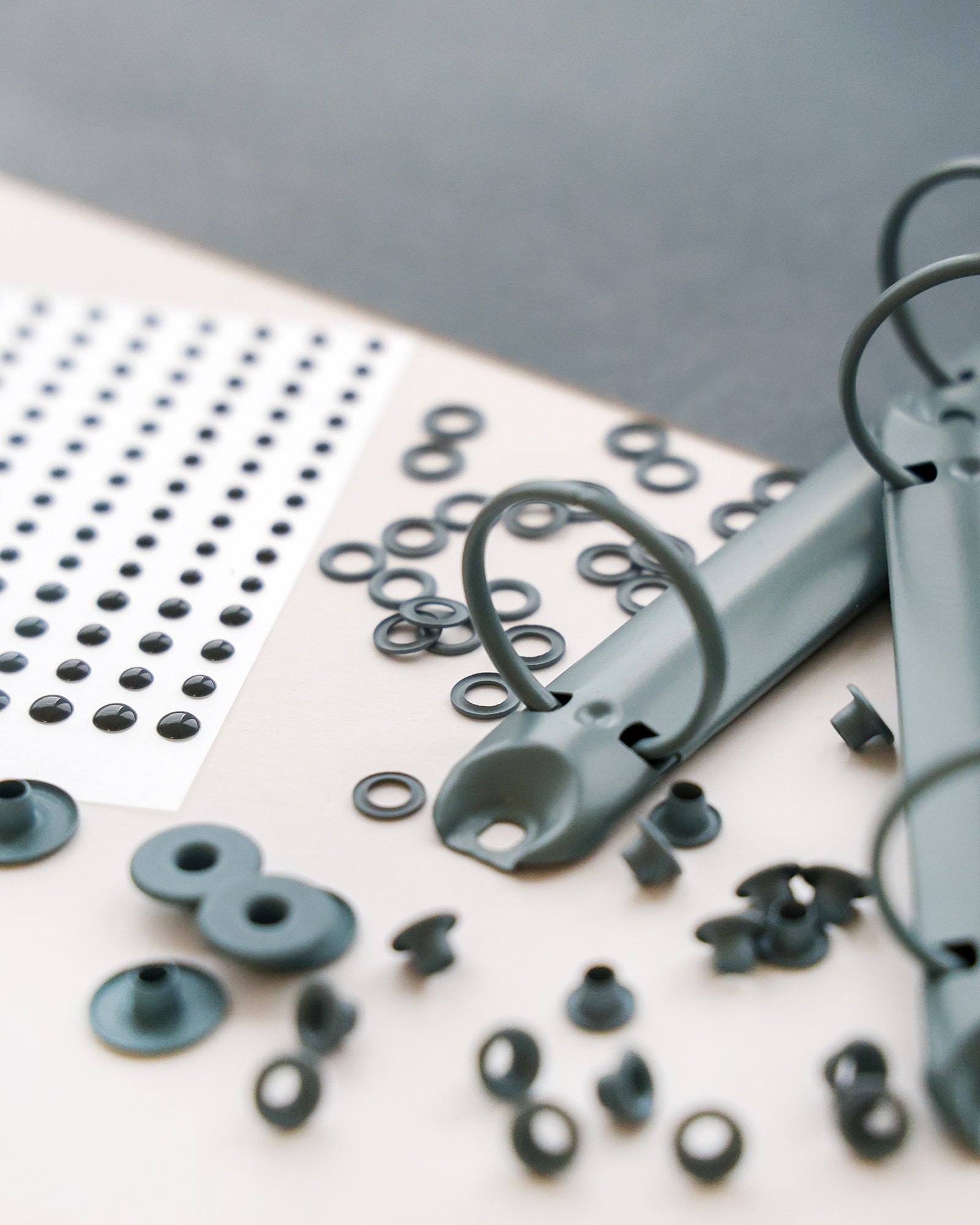 Nahaufnahme von Ordnerringen, schwarzen Aufklebern und kleinen runden Verschlüssen auf einem Schreibtisch.