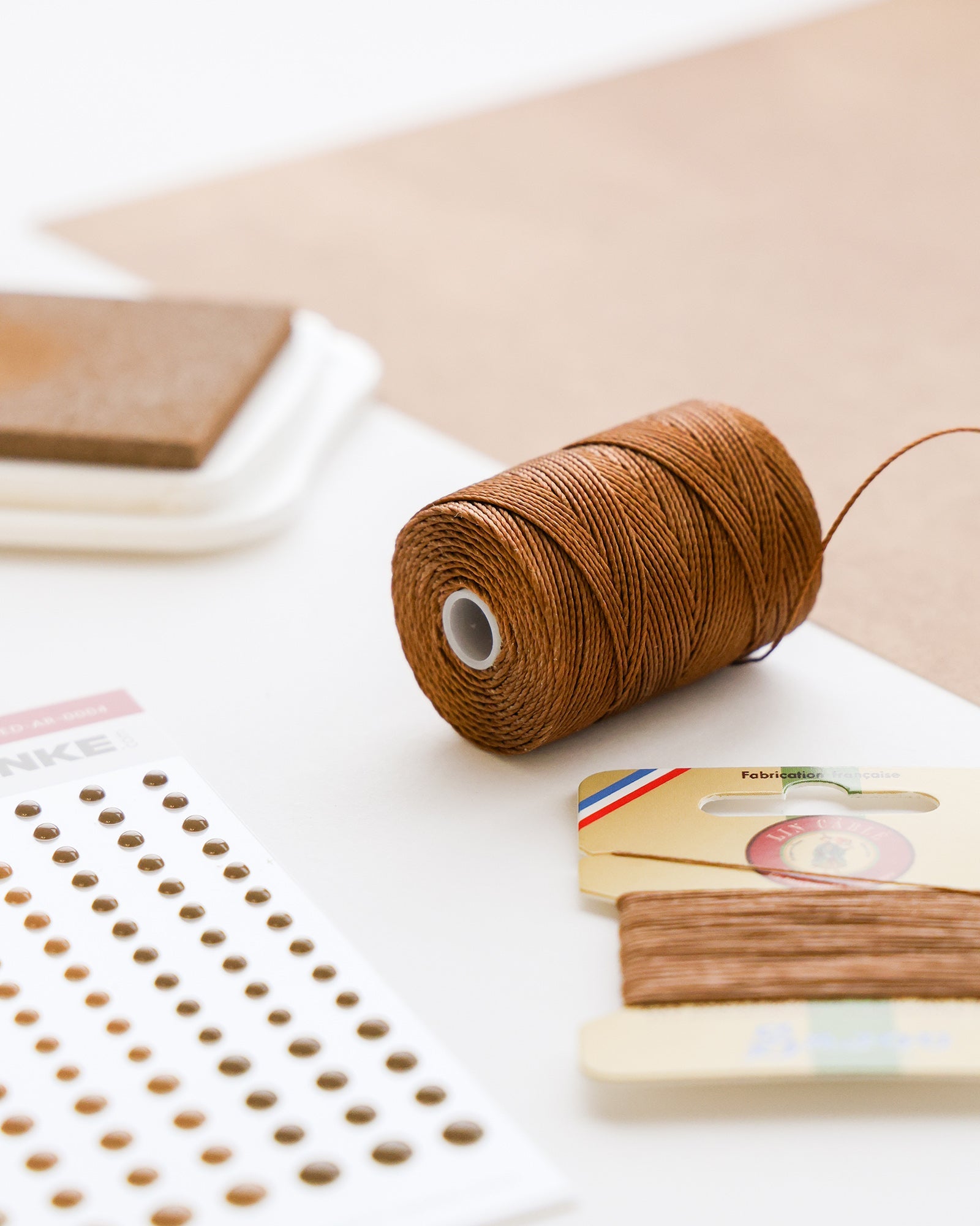 Braune Schnur auf einer Spule, mit Stickerpunkten und anderem Bastelmaterial auf einer weißen Fläche.