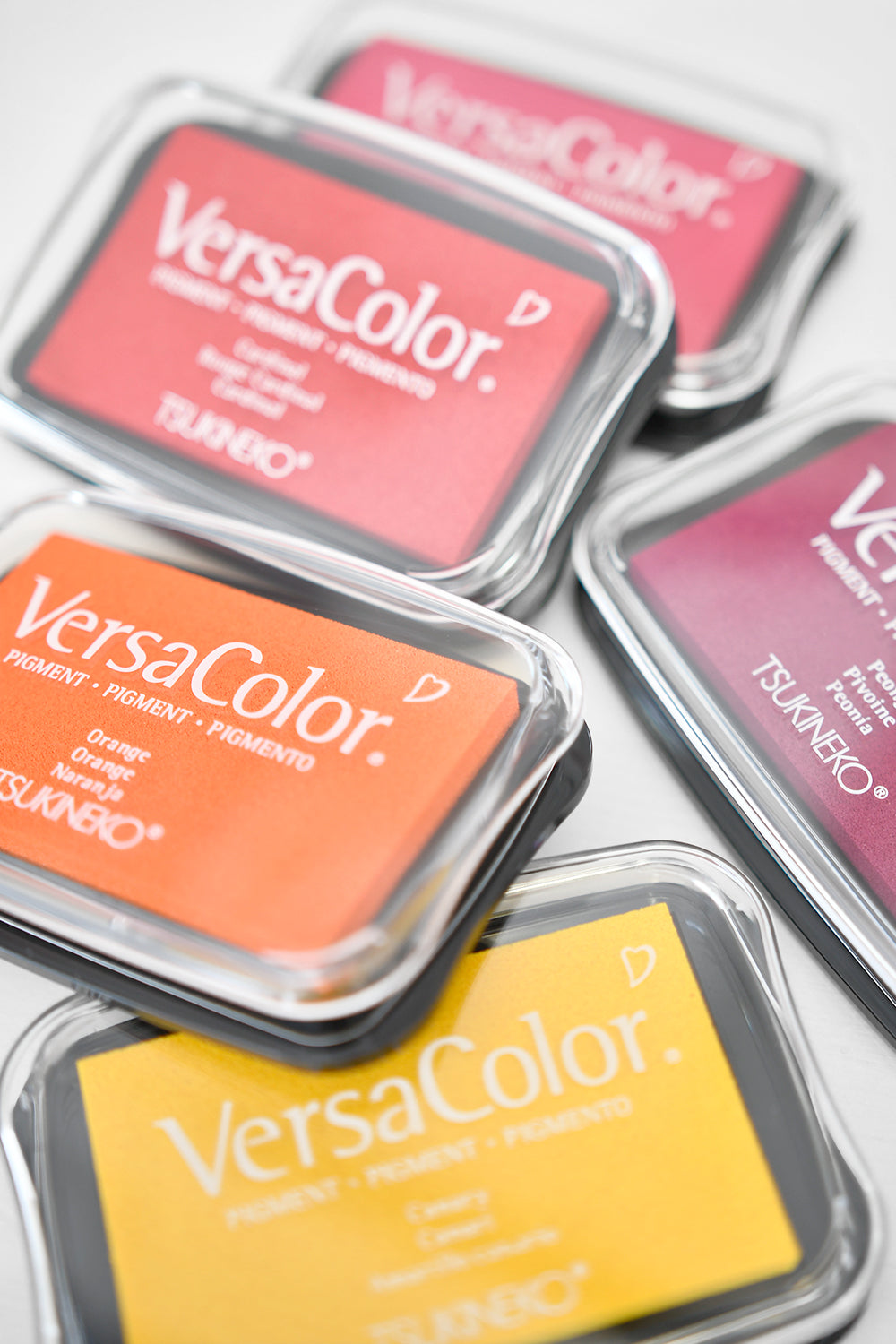 Fünf farbenfrohe VersaColor-Pigmenttintenkissen, darunter Orange, Pink und Gelb, angeordnet auf einer weißen Oberfläche.