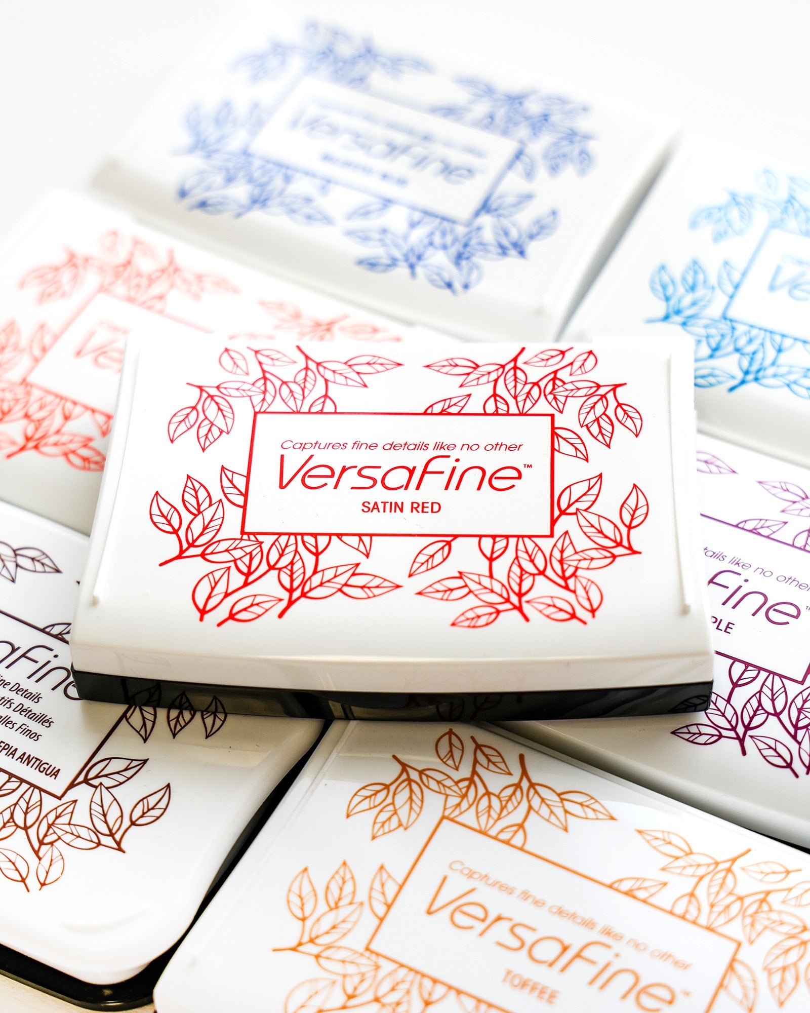 Nahaufnahme verschiedener VersaFine-Tintenkissen mit farbigen Blattmotiven auf weißen rechteckigen Behältern.