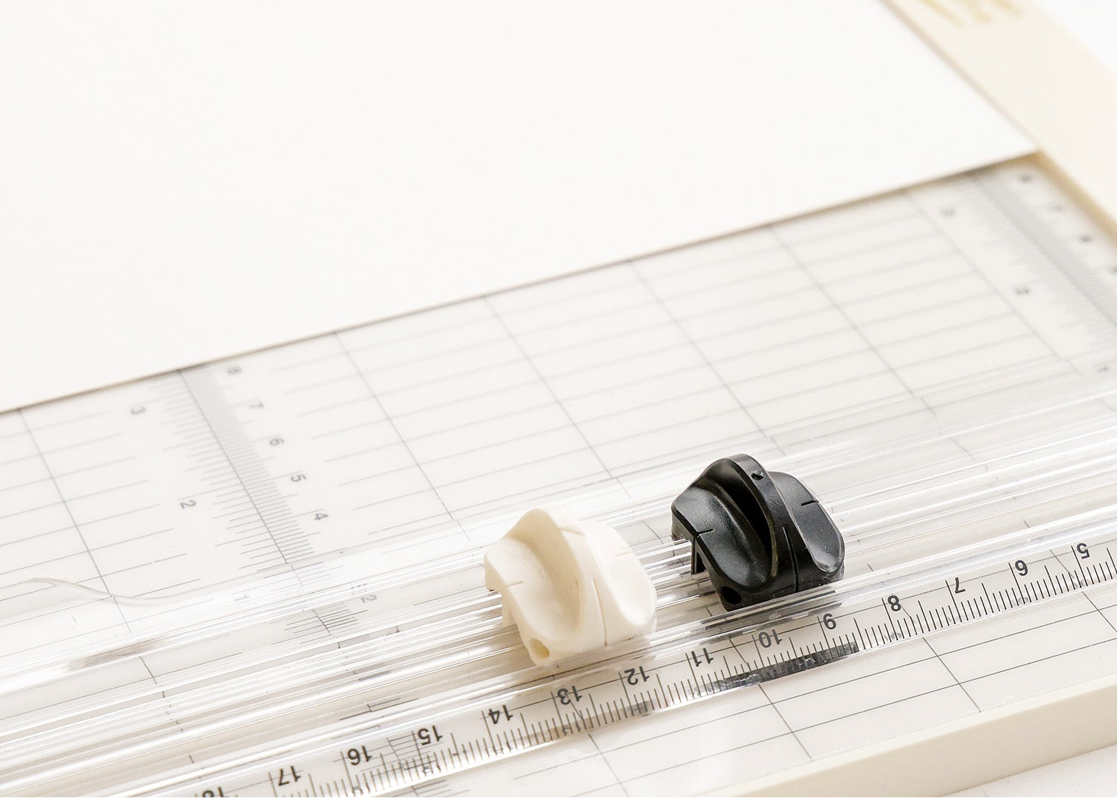 Ein Papierschneider mit einem klaren Lineal und schwarzen und weißen Gleitklingen auf einer hellen Oberfläche.