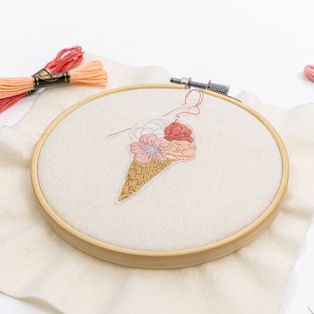 Stickerei einer blumigen Eistüte im Stickrahmen, gefertigt mit rosa Garn und Nadel auf weißem Stoff – eine inspirierende DIY-Stickerei oder einzigartige Stickvorlage von Alexandra Renke, perfekt, um Ihre Stickprojekte zu verschönern.