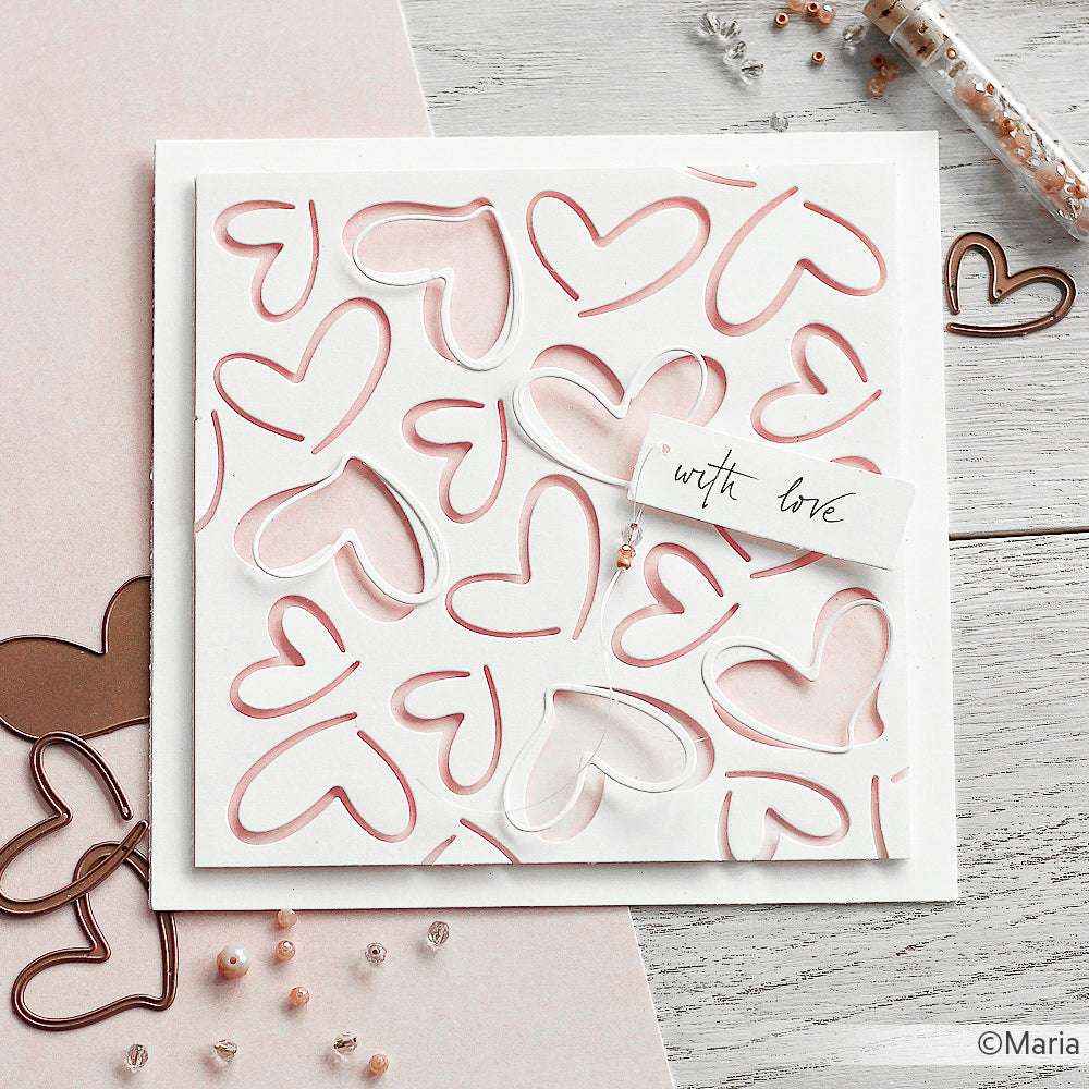 Eine handgefertigte Karte von Alexandra Renke mit rosa und weißen Herzausschnitten aus eleganten Designpapieren und einem "With Love"-Anhänger auf einer hellen Holzoberfläche.