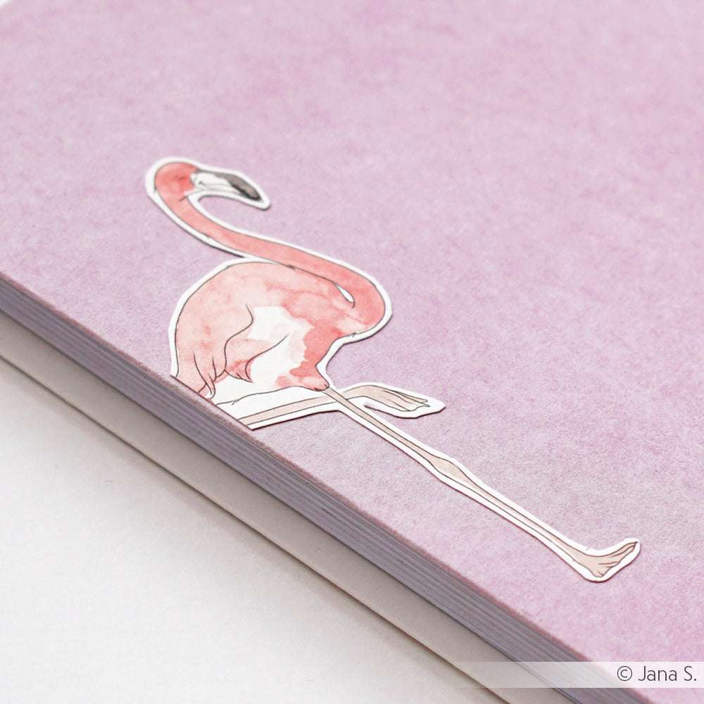 Ein rosafarbener Flamingo-Aufkleber von Alexandra Renke ziert die Ecke eines pastellfarbenen lila Notizbuchs und sorgt für eine verspielte Atmosphäre - perfekt für Ihre nächste Papierprojekte- oder Buchbinderei-Kreation.