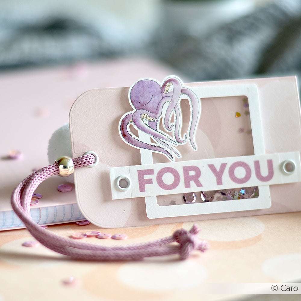 Rosa, handgefertigter Geschenkanhänger von Alexandra Renke aus Designpapier mit einem Oktopus-Aufkleber, dem Text "FOR YOU" und einer rosa Kordel mit Perle.