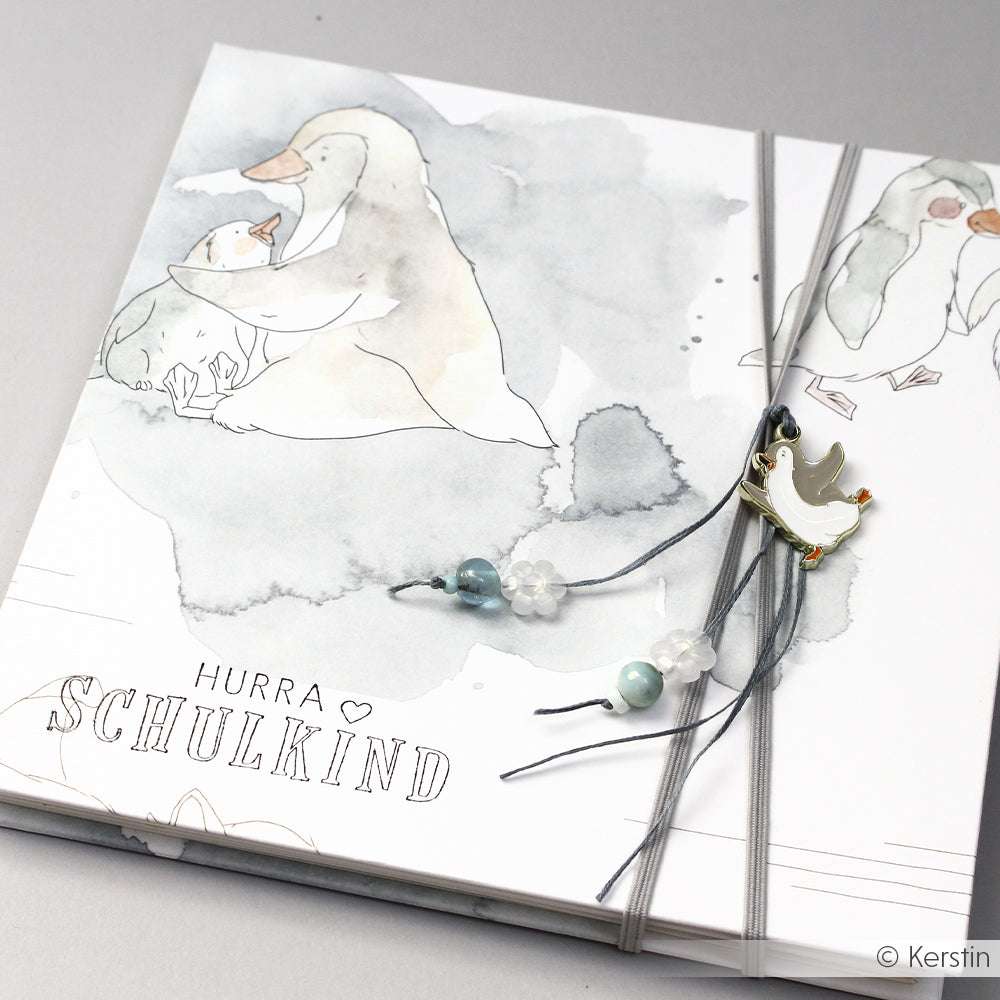 Quadratische Karte von Alexandra Renke mit einer Gänseillustration, Perlen und einem Gänseanhänger. Entworfen für kreative Papierprojekte mit dem Text "Hurra Schulkind".