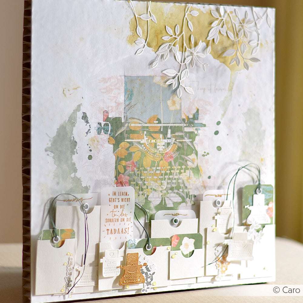 Eine mit Alexandra Renke Designpapier gestaltete Scrapbook-Seite mit einem alten Schreibmaschinenmotiv, Anhängern und geschichteten Papierblättern - eine ideale Inspiration für Papierprojekte und kreative Buchbinderei.