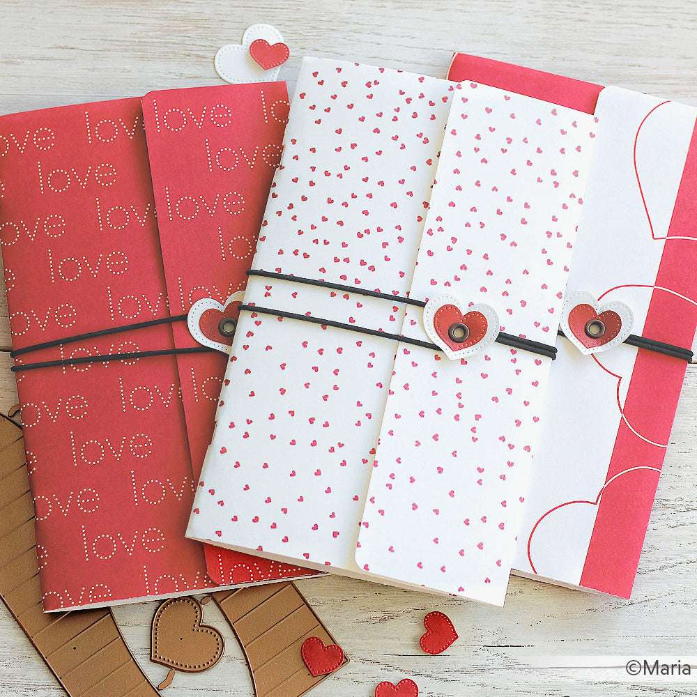 Drei gefaltete Valentinskarten mit Herzmotiven aus Alexandra Renke Herzgestöber Premiumrot Designpapier werden von schwarzen Bändern mit Herzakzenten auf weißer Oberfläche gehalten - ideal für Ihr nächstes Papierprojekt.