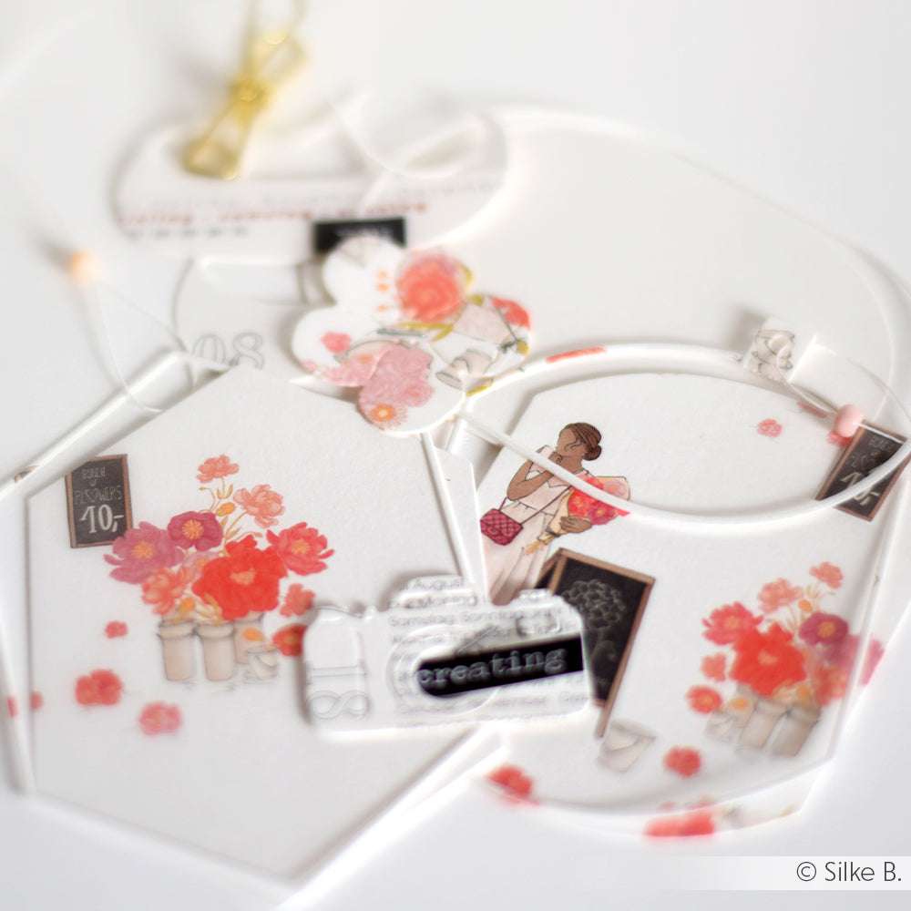 Mit Alexandra Renke Designpapier hergestellte Papierarbeiten zeigen florale Muster, eine Mädchenillustration und Vintage-Verzierungen, die alle auf einer weißen Oberfläche angeordnet sind.