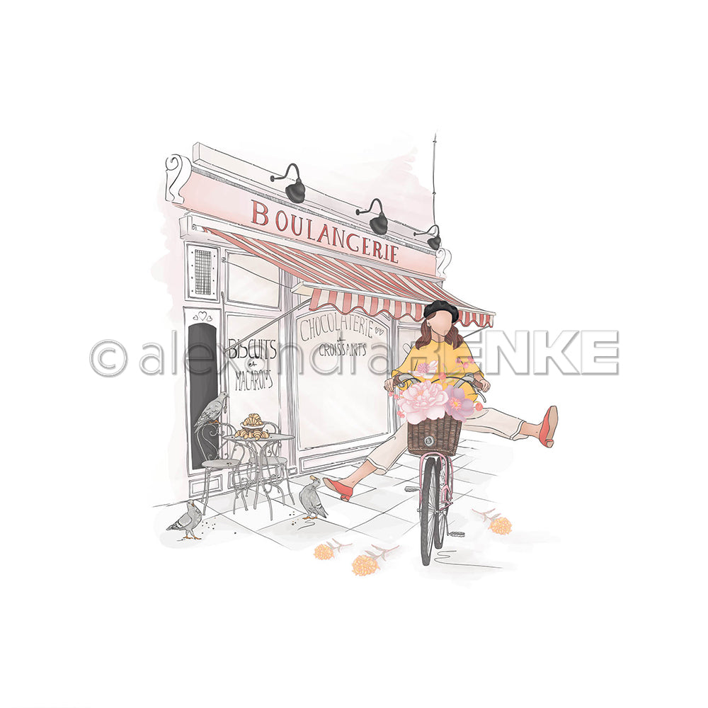 Eine Frau fährt mit einem Fahrrad mit Blumen an einer französischen Bäckerei vorbei, während Vögel auf dem Bürgersteig neben einer Buchbinderei mit buntem Alexandra Renke Designpapier im Schaufenster Krümel fressen.