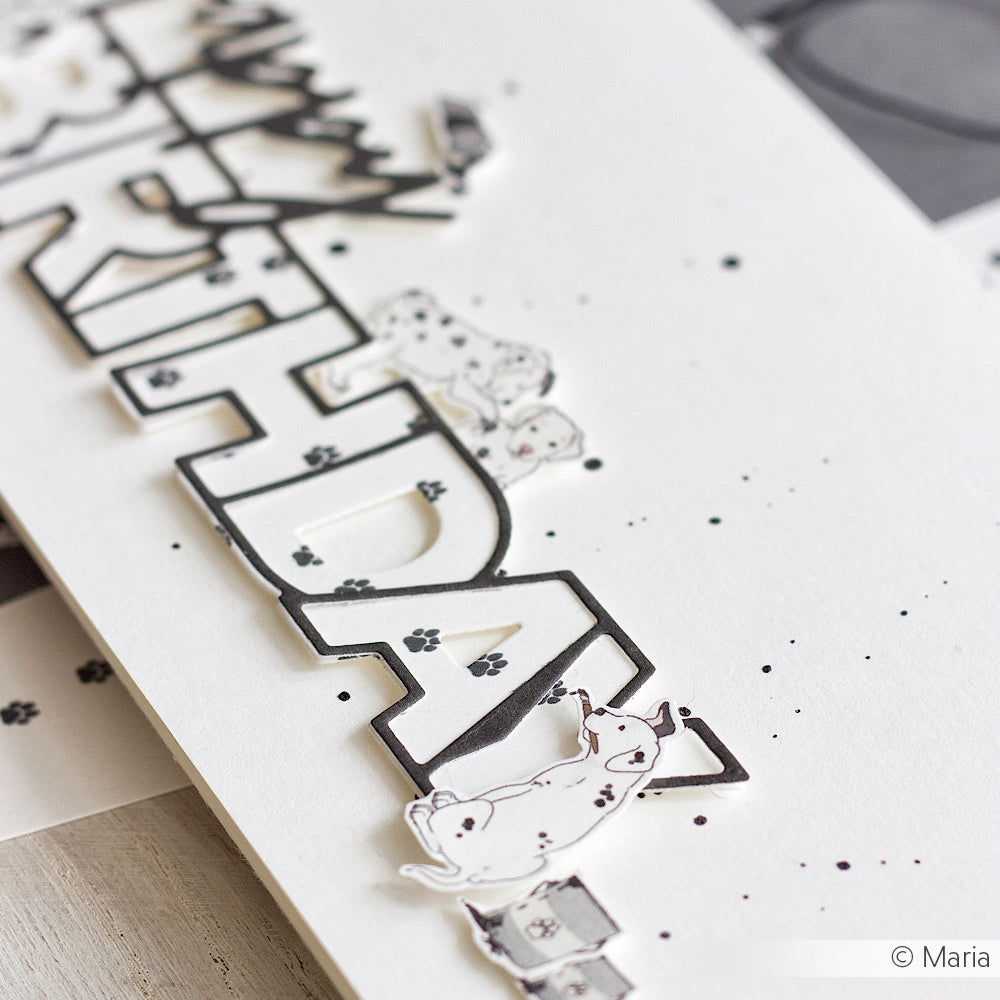 Nahaufnahme einer handgefertigten Geburtstagskarte, die mit Alexandra Renke Designpapier hergestellt wurde - RTHDAY in fetten Buchstaben, verziert mit kleinen illustrierten Hunden und Pfotenabdrücken.