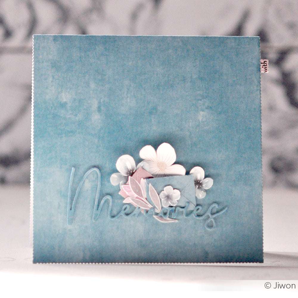 Quadratische blaue Karte von Alexandra Renke mit dem Text "Memories" und weißen Blumen in der Mitte; ideal für Papierprojekte oder Buchbinderei, mit einem weichen, künstlerischen Hintergrund und eleganten Designpapier-Akzenten.