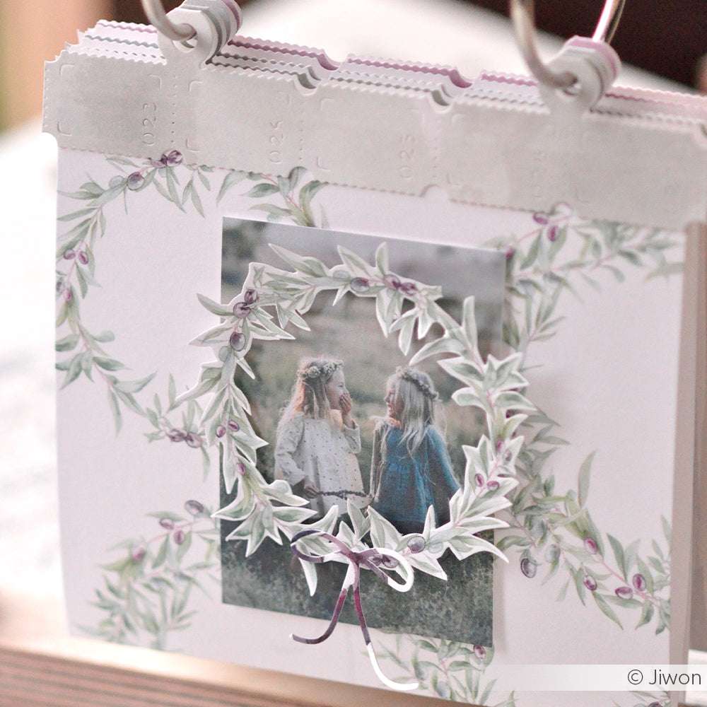 Ein dekoratives Kalenderblatt von Alexandra Renke mit einem Foto von zwei Mädchen, umrahmt von Olivenkränzen und bezauberndem Designerpapier - ideal zum Basteln mit Papier.