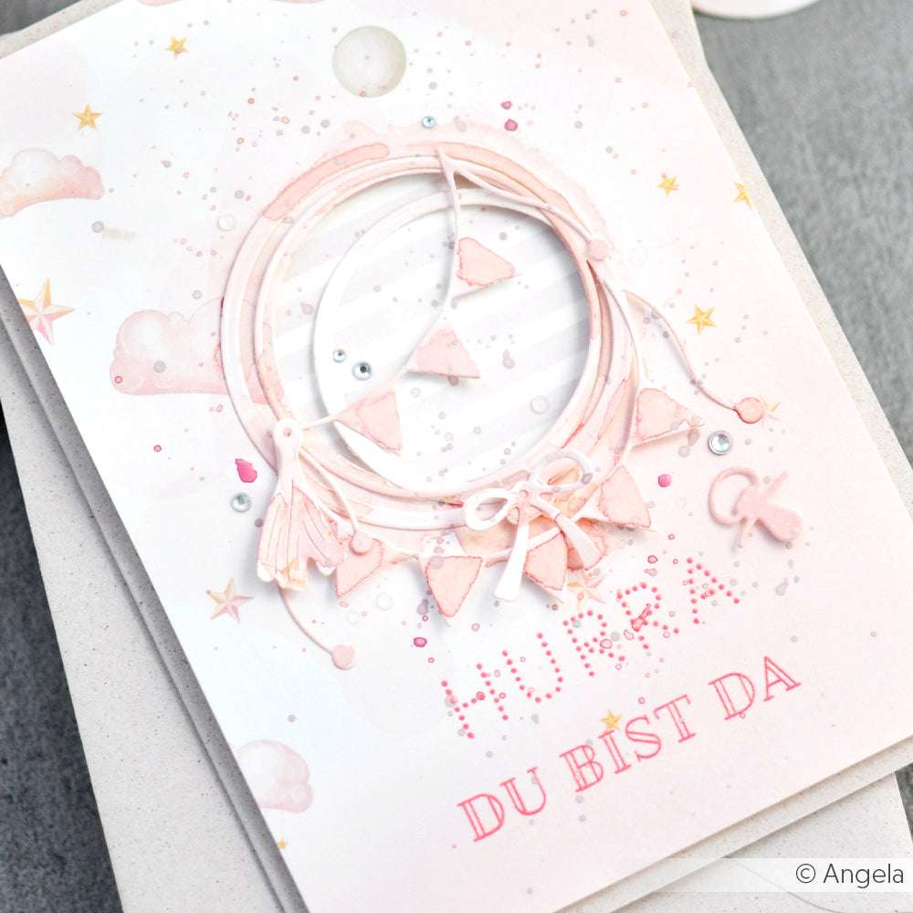 Rosa-weiße Karte von Alexandra Renke mit Kranz, Wimpeln, Sternen und dem Text "Hurra du bist da" - ideal für Papierprojekte oder die Verwendung mit Designpapier.