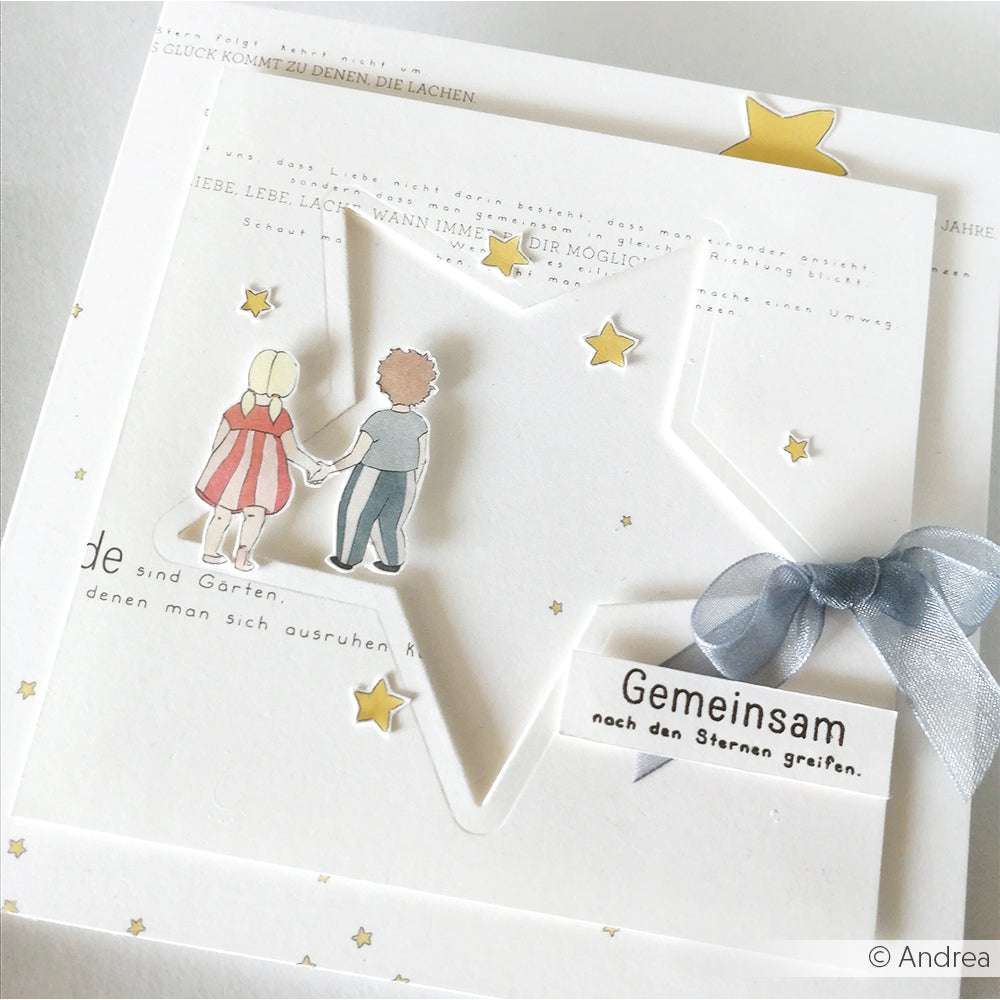 Handgefertigte Karte von Alexandra Renke aus Designpapier mit einem ausgeschnittenen Stern, zwei Kindern, die sich an den Händen halten, zarten Sternen und einem Band mit deutscher Botschaft - ideal für Ihre Papierprojekte.