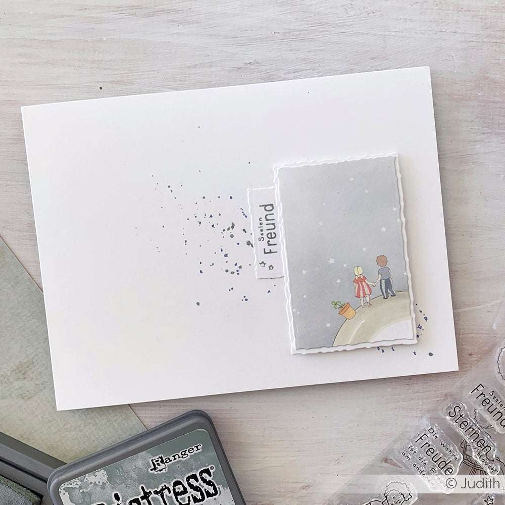 Handgefertigte Karte von Alexandra Renke mit zwei Kindern auf einem Hügel, hergestellt mit Designpapier aus der Kollektion Kärtchenbogen Sternenfreunde und mit einem "Freund"-Anhänger versehen. Ideal für Papierprojekte und herzliche Grüße.