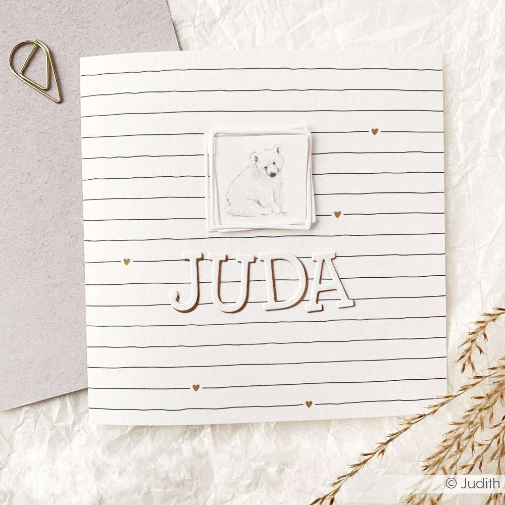 Quadratische Grußkarten von Alexandra Renke mit Polarbär-Illustration und dem Namen JUDA auf liniertem Designpapier, verziert mit kleinen goldenen Herzen.