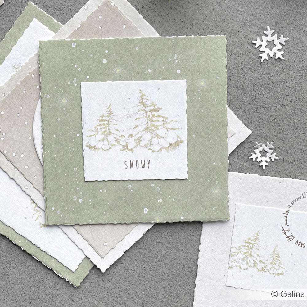 Ein Stapel Winterkarten von Alexandra Renke, gestaltet mit Designpapier mit Motiven von Wintertannen im Schnee und zarten Schneeflockenausschnitten - ideal für festliche Papierprojekte.