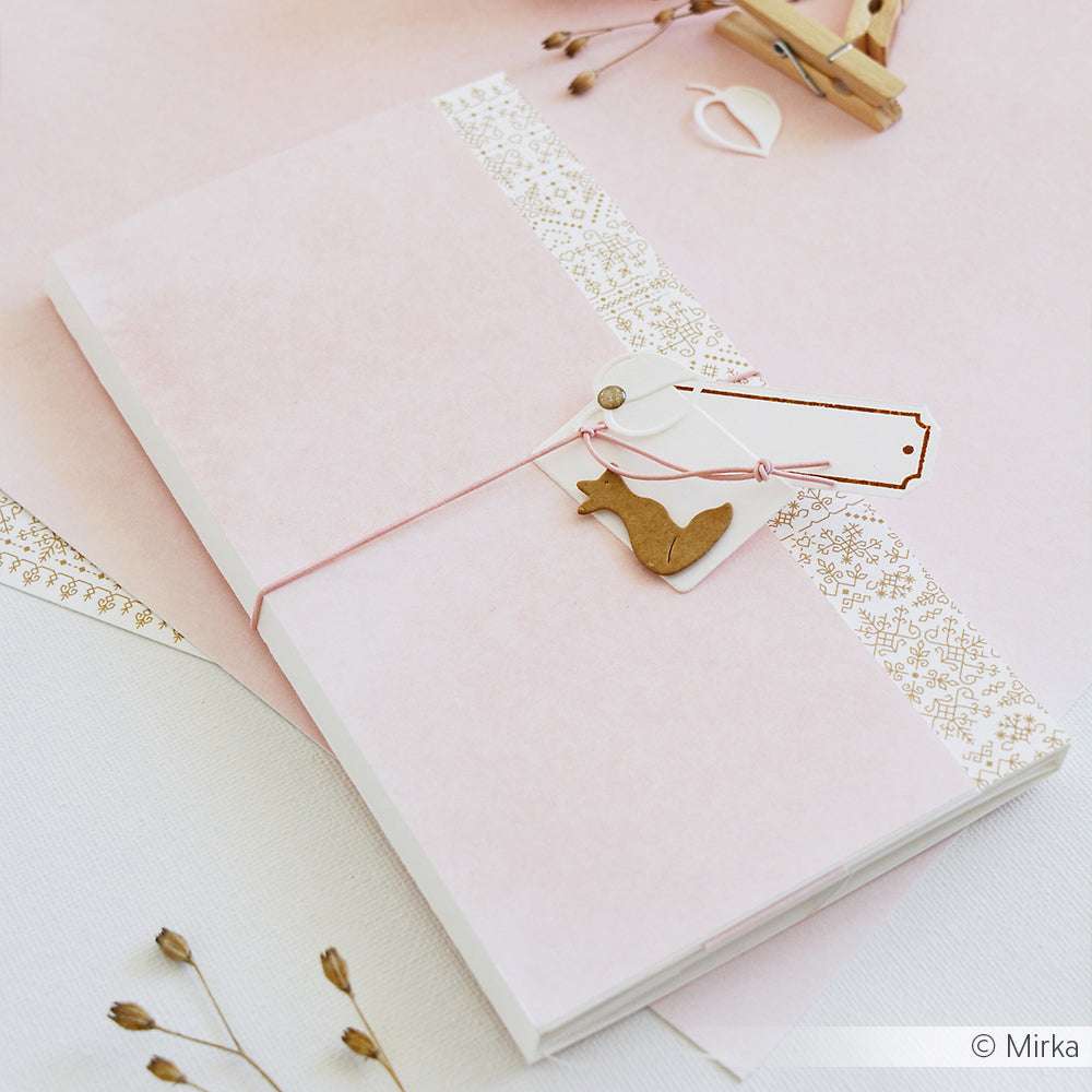 Eine handgefertigte rosa-weiße Karte von Alexandra Renke, hergestellt mit Designpapier und verziert mit einem Vogelanhänger, Bindfaden und getrockneten Blumen auf einem weichen Hintergrund.