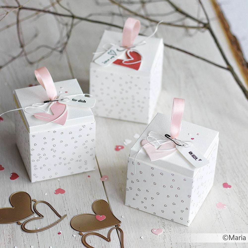 Drei weiße Alexandra Renke Geschenkboxen mit rosa Schleifenhenkeln, Herzanhängern und Herzkonfetti - ideal für Papierprojekte oder in Kombination mit Herzgestöber Gold Outline Designpapier.