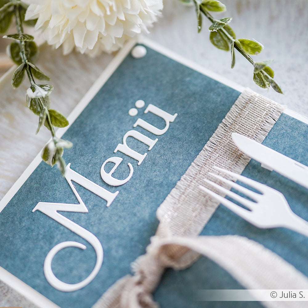 Die blaue Menükarte von Alexandra Renke ist mit weißem Text, einem Besteckmotiv, floralen Akzenten und einer Schleife auf hochwertigem Designpapier ausgestattet - ideal für anspruchsvolle Papierprojekte.