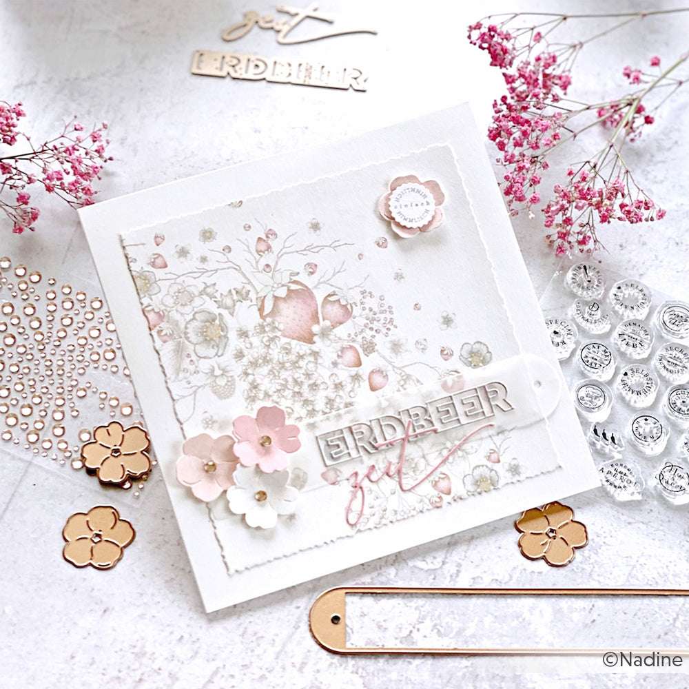 Eine handgefertigte Blumenkarte von Alexandra Renke mit dem Text "ERDBEER" inmitten von rosa Blumen und Bastelmaterial - ideal für Papierprojekte oder als Inspiration für Ihre nächste Kreation mit Designpapier Erdbeerblütenkranz.
