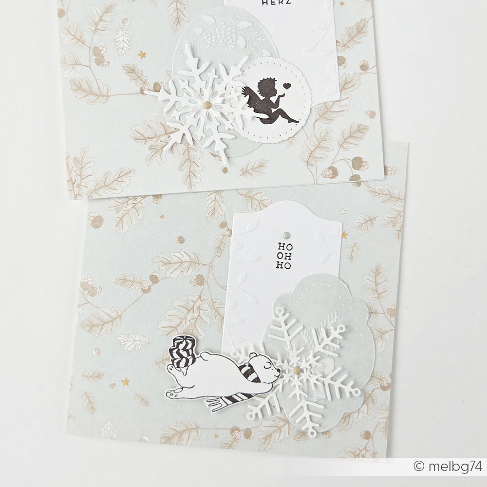 Zwei Weihnachtskarten mit Motiven wie Schneeflocken, Engeln und Eisbären auf salbeigrünem Papier.