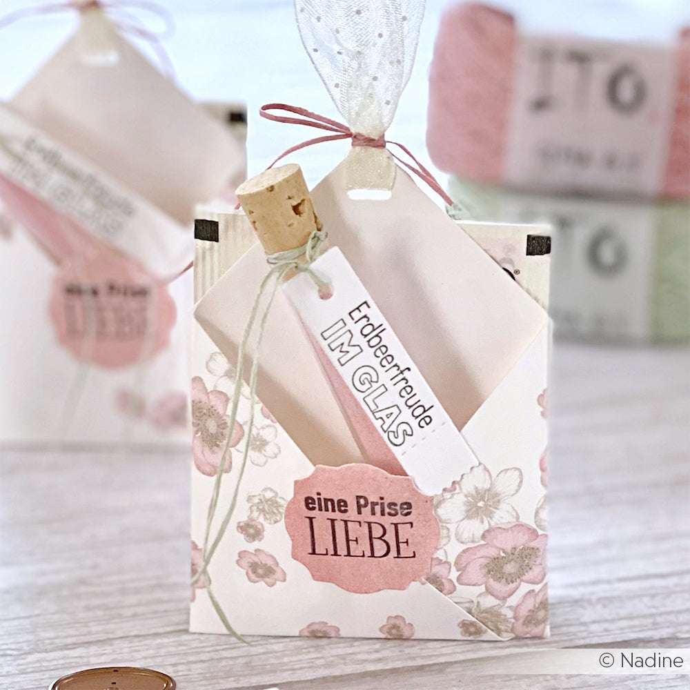 Dekorative Geschenktüte von Alexandra Renke aus Designpapier mit floralem Muster, einem Anhänger mit der Aufschrift "eine Prise LIEBE", einer Notiz und einem kleinen Korken - ideal für kreative Papierprojekte.