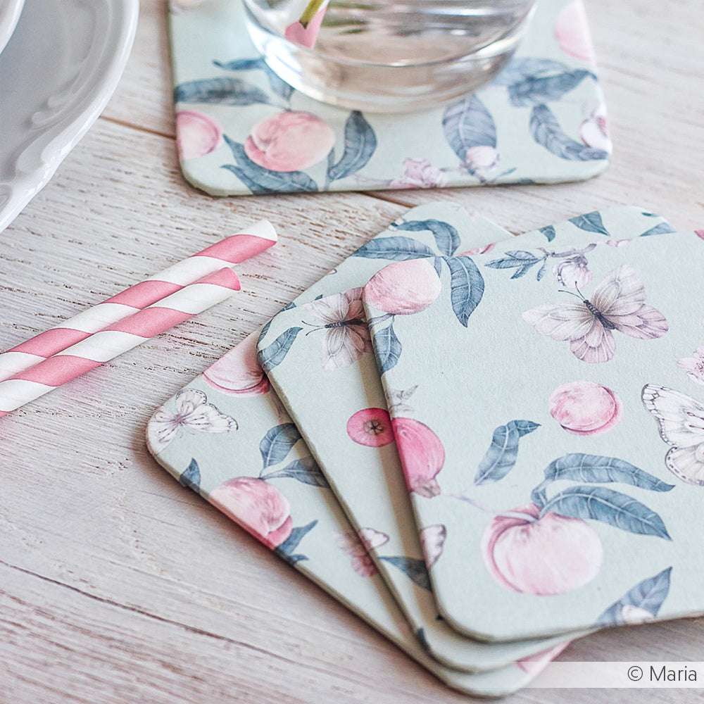 Drei farbenfrohe Designpapier-Untersetzer von Alexandra Renke mit Obst- und Schmetterlingsmotiven werden mit einem Glas und rosa gestreiften Strohhalmen gezeigt - die perfekten Akzente für Ihre Papierprojekte.