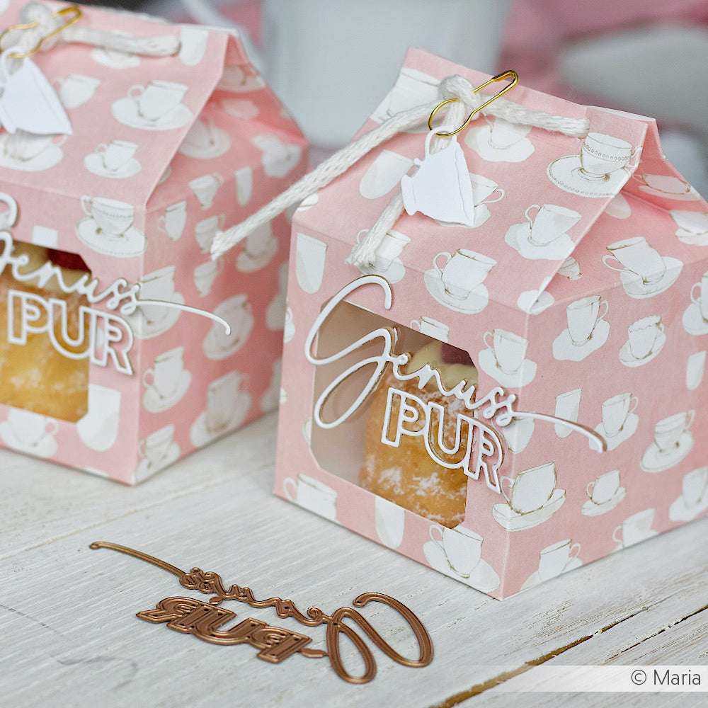 Zwei rosafarbene Geschenkboxen mit Teetassenmustern und dem Text "Genuss Pur" von Alexandra Renke aus stilvollem Designpapier stehen auf einer weißen Holzfläche - ideal für Grußkarten oder Papierprojekte.