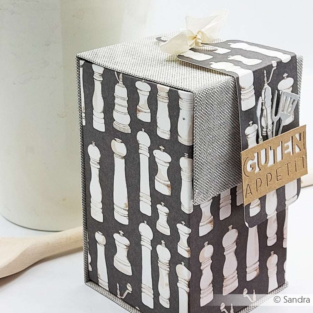 Geschenkschachtel von Alexandra Renke mit Pfeffermühlenmuster auf hochwertigem Designpapier, verziert mit einer beigen Schleife und dem Anhänger "GUTEN APPETIT". Perfekt für Papierprojekte oder als süße Grußkarten-Verpackung. Abgebildet auf einer weißen Oberfläche.
