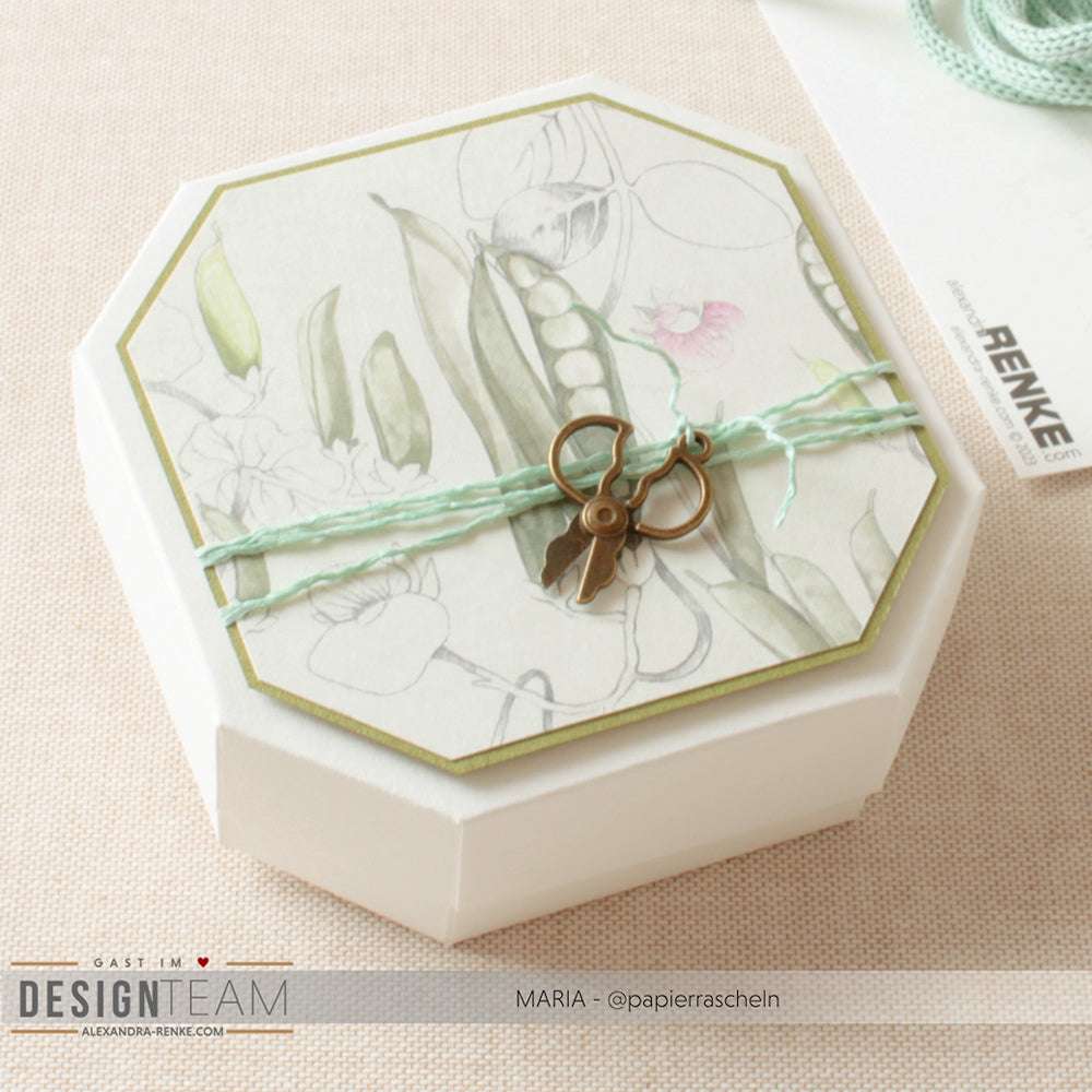 Die achteckige Geschenkbox von Alexandra Renke ist mit einem floralen Designpapier-Deckel, einer mintfarbenen Schnur und einem Scherenanhänger ausgestattet - ideal für Papierprojekte oder Grußkarten auf hellem Grund.