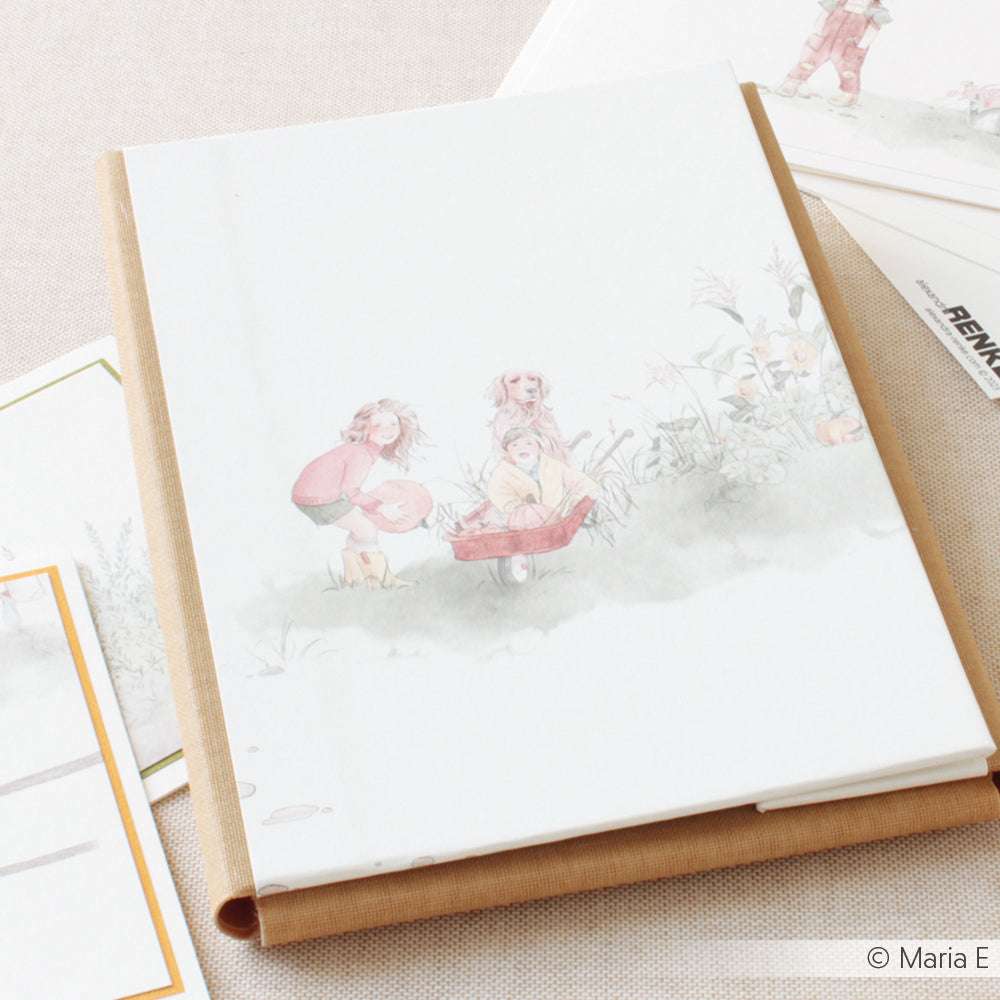 Ein Notizbuch von Alexandra Renke, auf dessen Cover spielende Kinder im Freien abgebildet sind, weckt Sommerfreude Gemüsebeet-Vibes, die auf einer hellen Oberfläche mit verstreutem Designpapier und Papieren präsentiert werden.