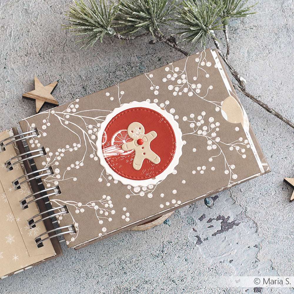 Ein festliches Notizbuch von Alexandra Renke mit einem Lebkuchenmann und einem weißen Beerenmotiv auf Premiumrot Designpapier, das neben Tannenzweigen abgebildet ist - perfekt für Ihre weihnachtlichen Papierprojekte.