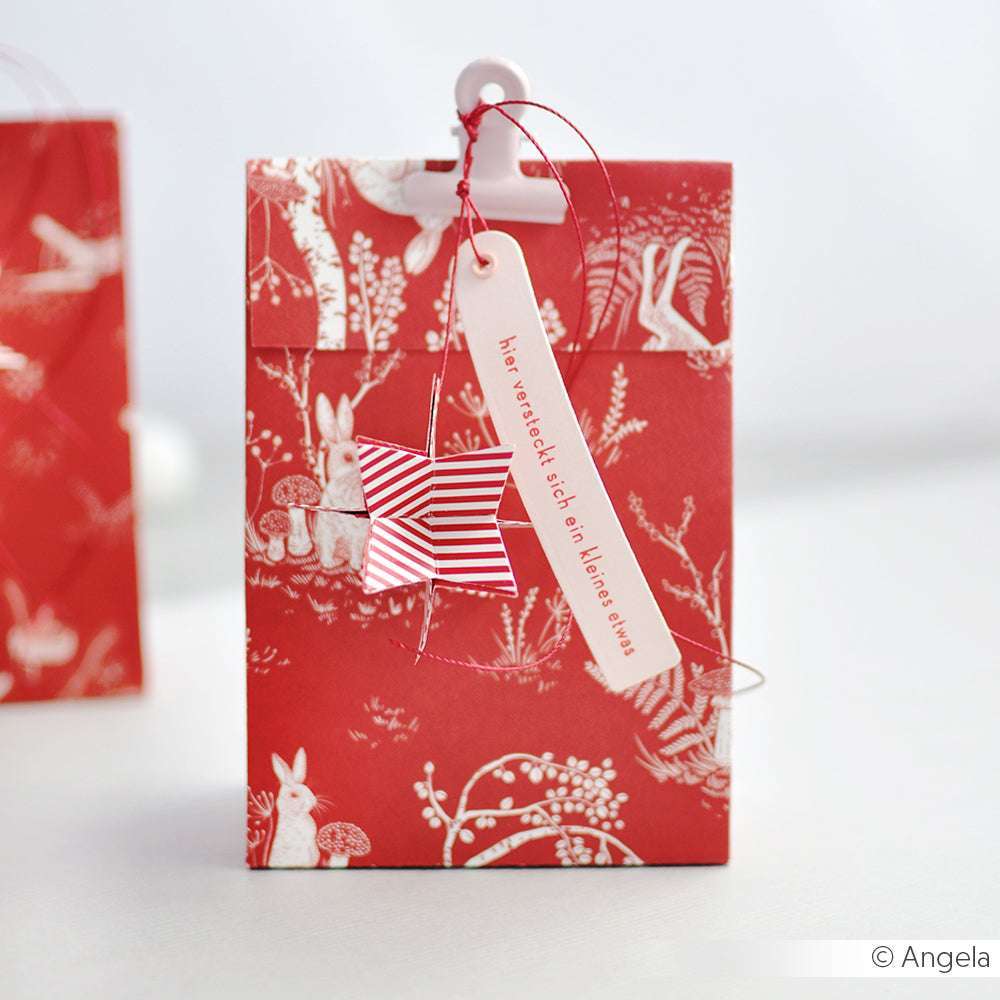Rote Geschenktüte von Alexandra Renke aus Premiumrot Designpapier mit weißen Tier- und Pflanzenmotiven, einem Stern-Ornament und einem deutschen Anhänger - ideal für Ihre festlichen Papierprojekte.
