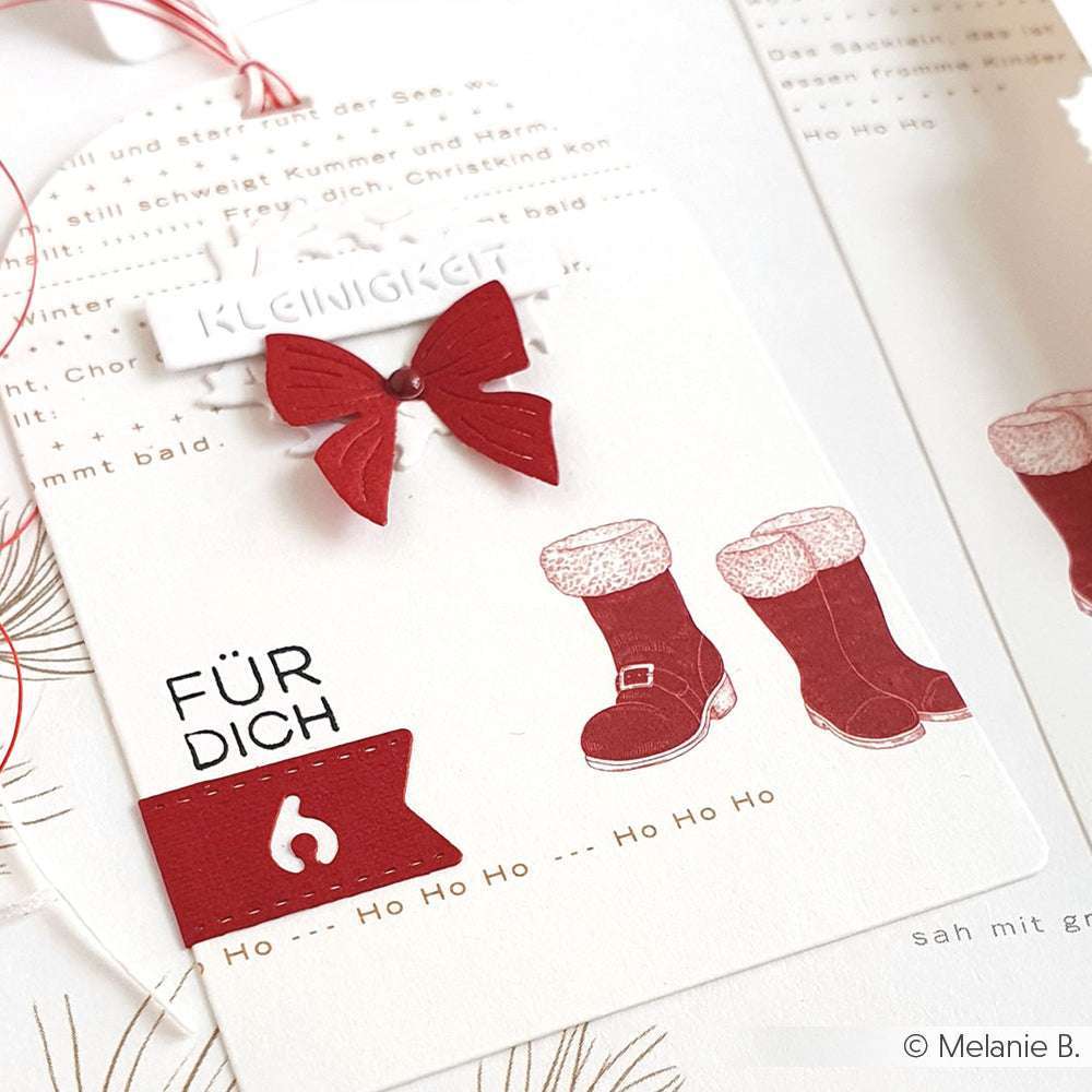 Eine Weihnachtskarte von Alexandra Renke in Premiumrot zeigt rote Stiefel, eine rote Schleife und den deutschen Text "FÜR DICH" und "Ho Ho Ho" auf Weiß - ein elegantes Winterdesign.