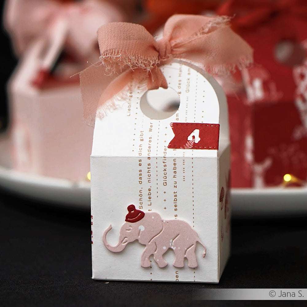 Weiße Geschenkbox mit rosa Schleife, roter Flagge #4 und einem rosa Elefanten mit rotem Hut von Alexandra Renke - ideal für Papierprojekte oder als Inspiration für Buchbinderei und kreative Designpapier-Basteleien.