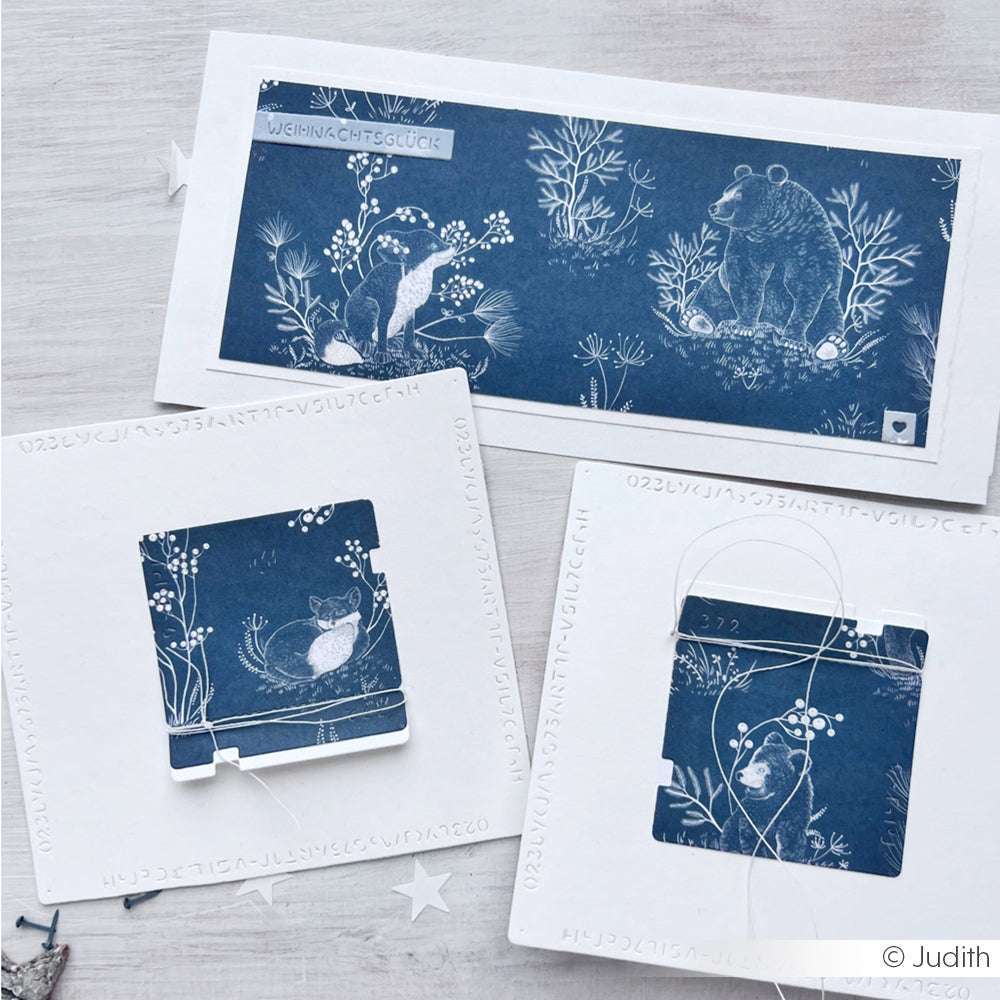 Drei weiß-blaue Grußkarten von Alexandra Renke, verziert mit Waldtier- und Naturmotiven, sind auf einem hellen Untergrund abgebildet - ideal für Ihre winterlichen Papierprojekte oder kreativen Designpapier-Anwendungen.