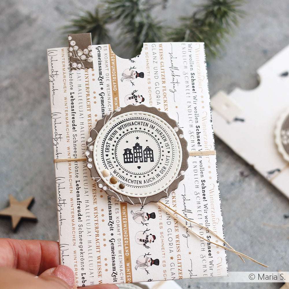 Eine festliche, handgefertigte Weihnachtskarte mit Alexandra Renke Designpapier und Schnur, mit deutschem Text und charmanten Papierprojekte-Details in der Hand.